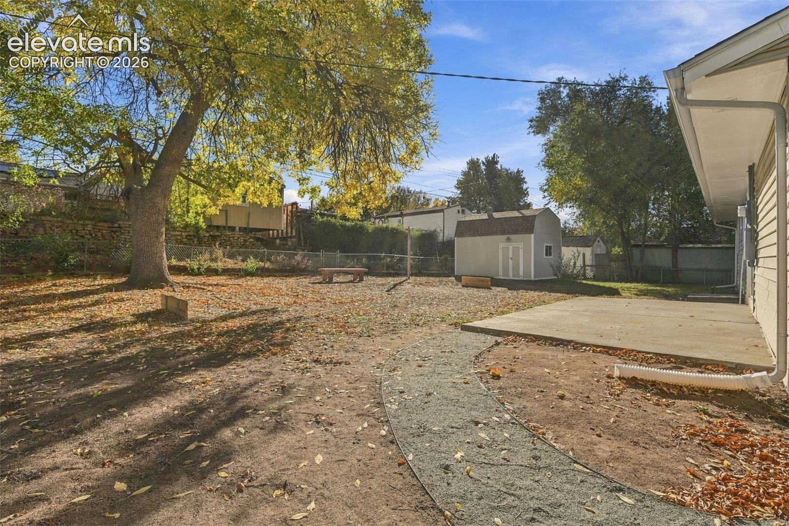 Backyard featuring a concrete patio, gravel pathway, detached storage shed, and mature trees
