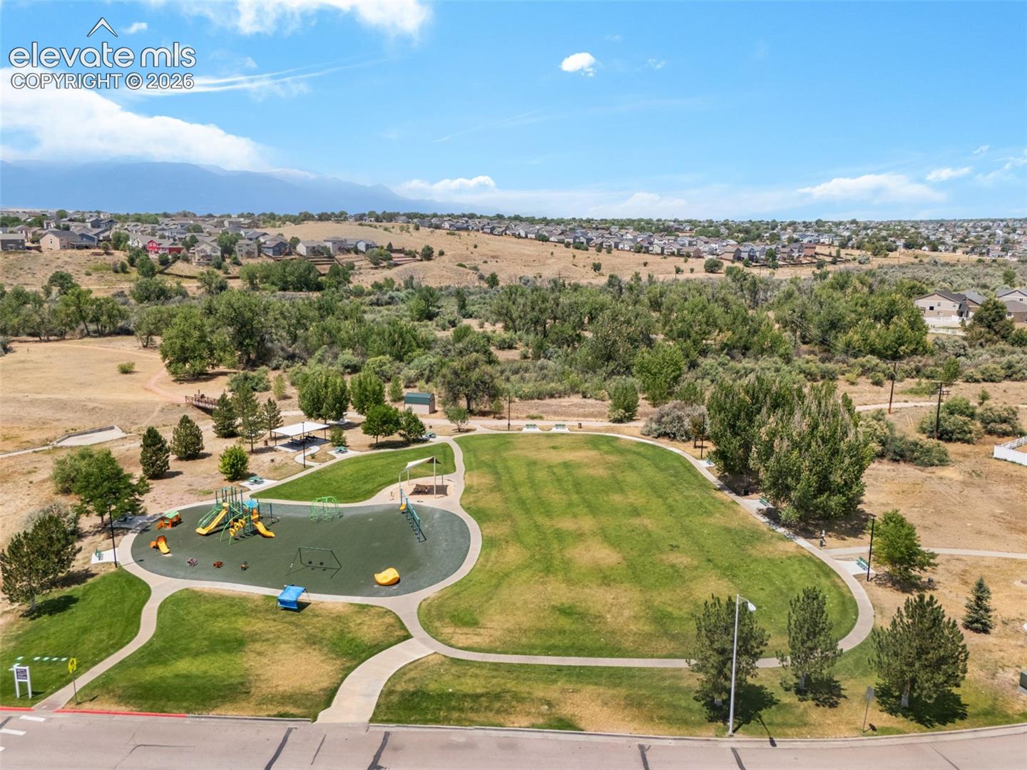Expansive green space featuring a playground with multiple slides, paved pathways, and mature trees