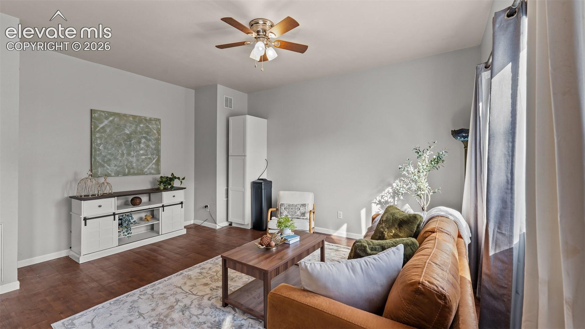 Hardwood-finish flooring, light gray wall tones, ceiling fan, and window with drapes
