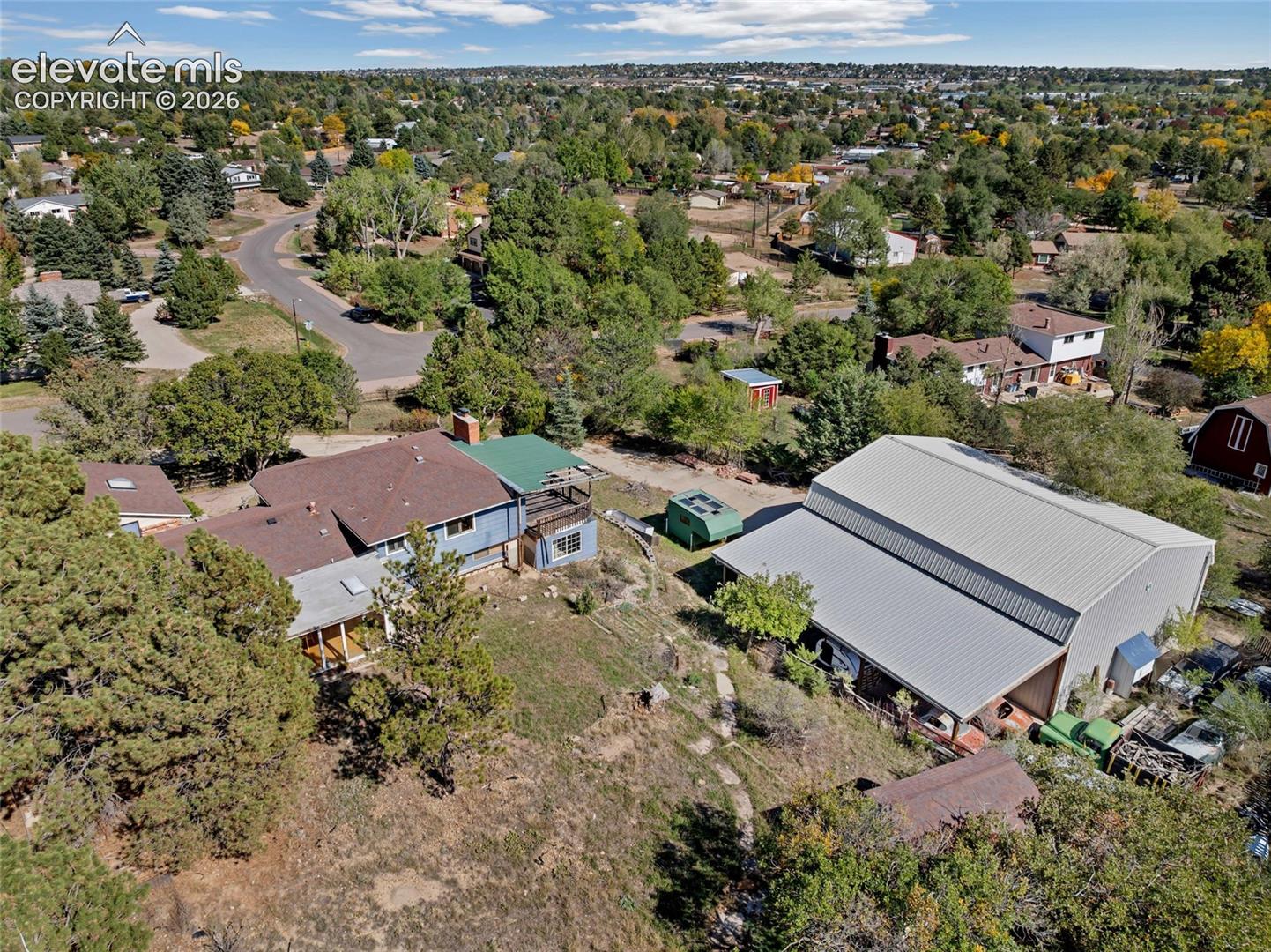 Expansive property featuring a large metal-sided outbuilding, a multi-level residence with a covered porch, and mature trees
