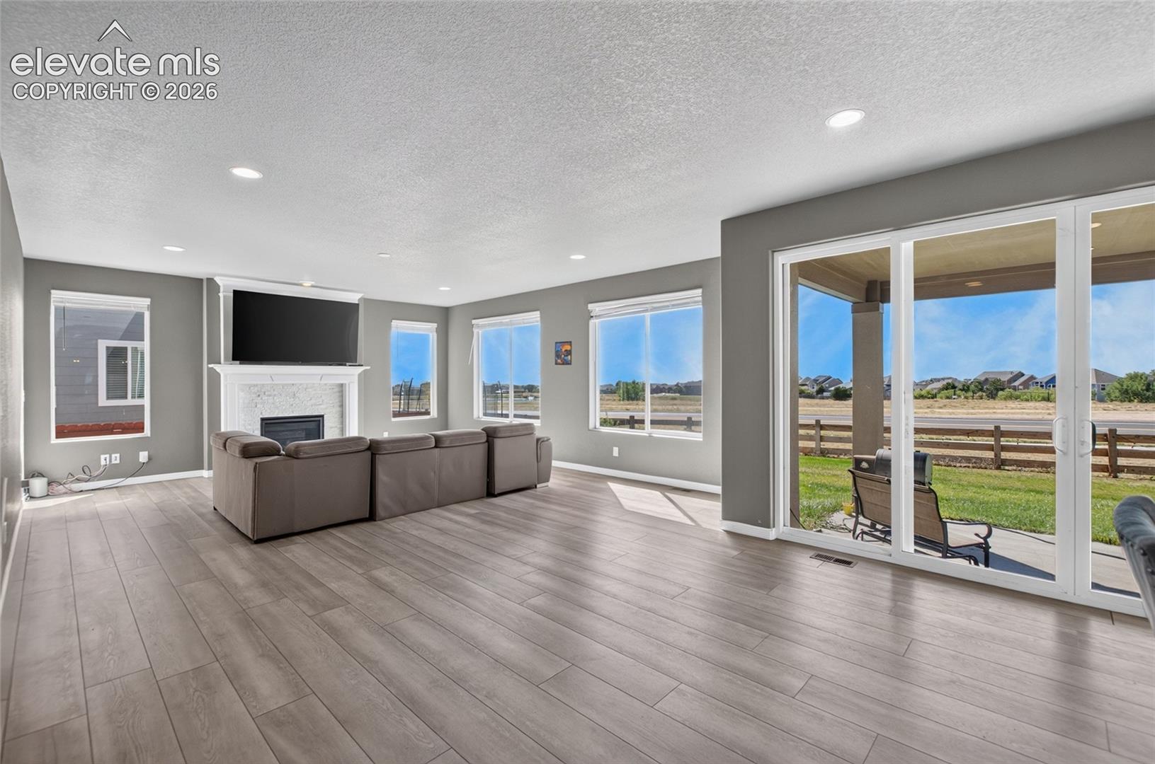 Spacious living area featuring wood-finish flooring, recessed lighting, and a fireplace with a white mantel
