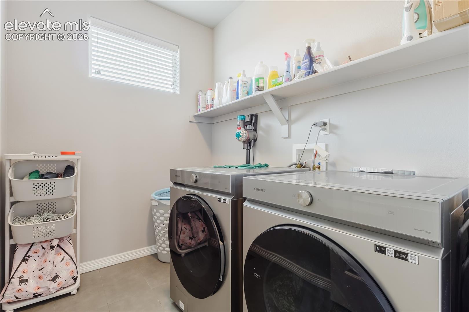 Dedicated laundry space featuring a window with horizontal blinds, built-in wall shelving, and concrete-finish flooring