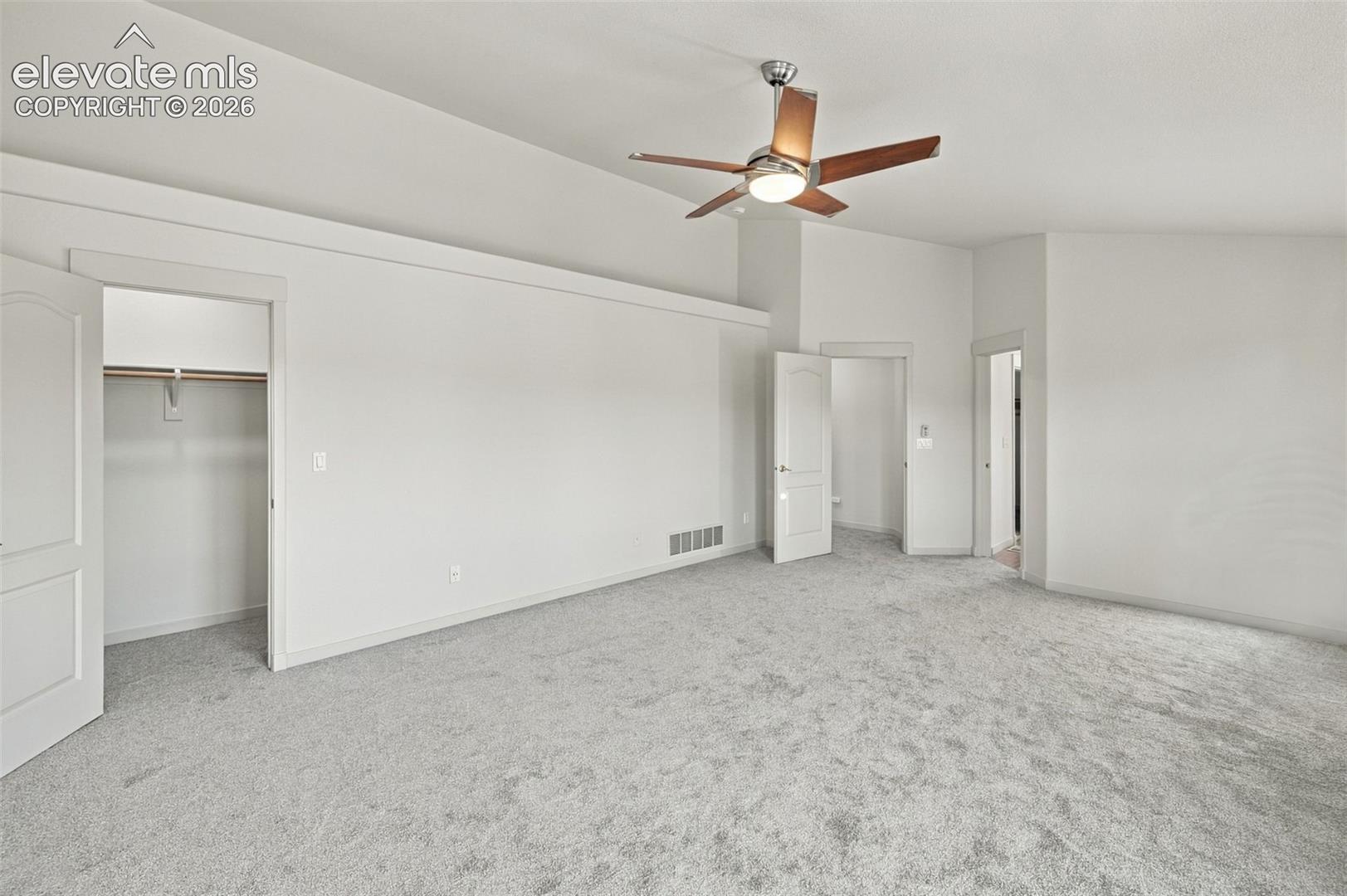 Vaulted ceilings, neutral carpeting, ceiling fan with integrated lighting, and multiple reach-in closet spaces with built-in shelving