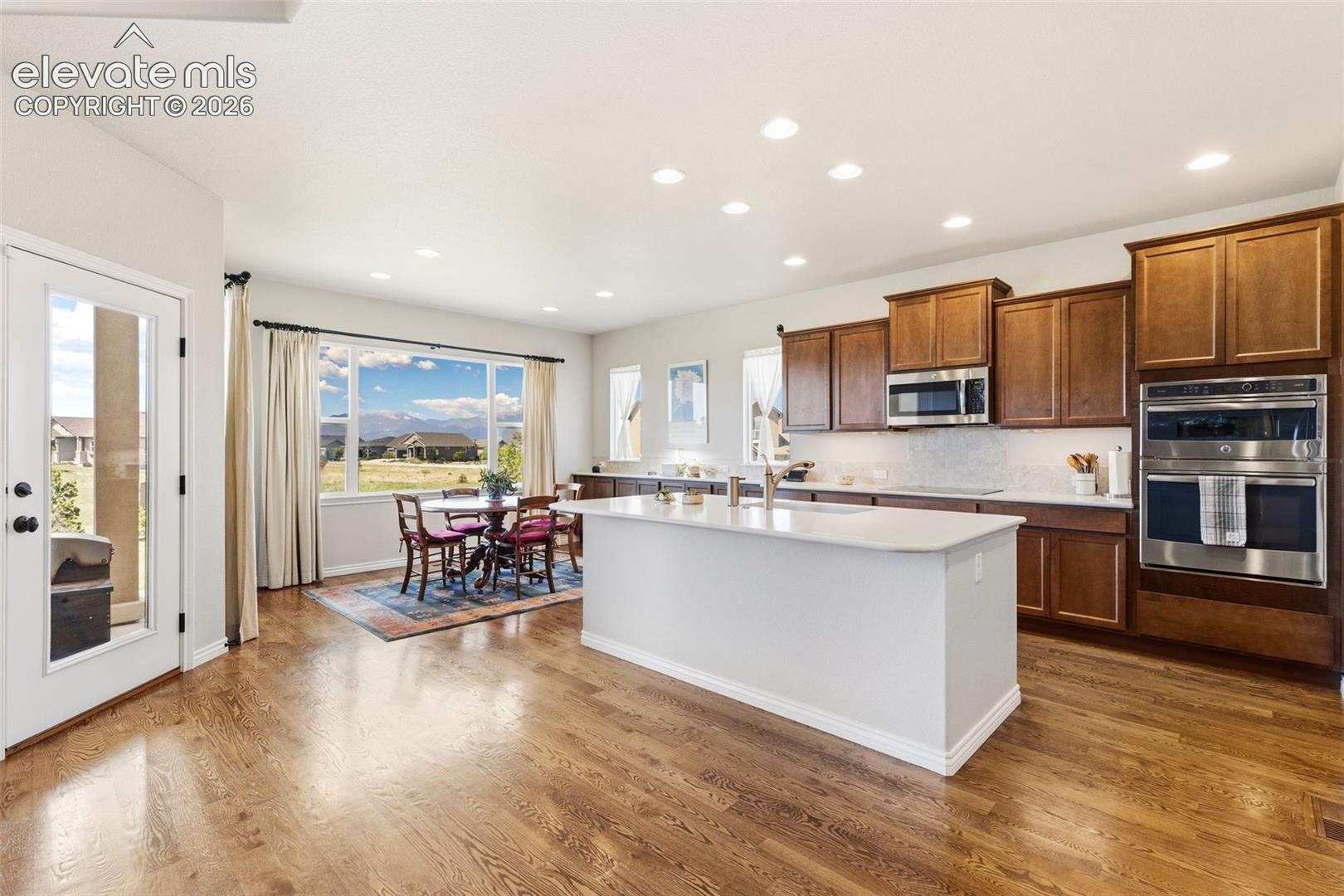 Open floor plan of kitchen and eat-in area featuring mountain views, hardwood flooring, stainless appliances, quartz counters