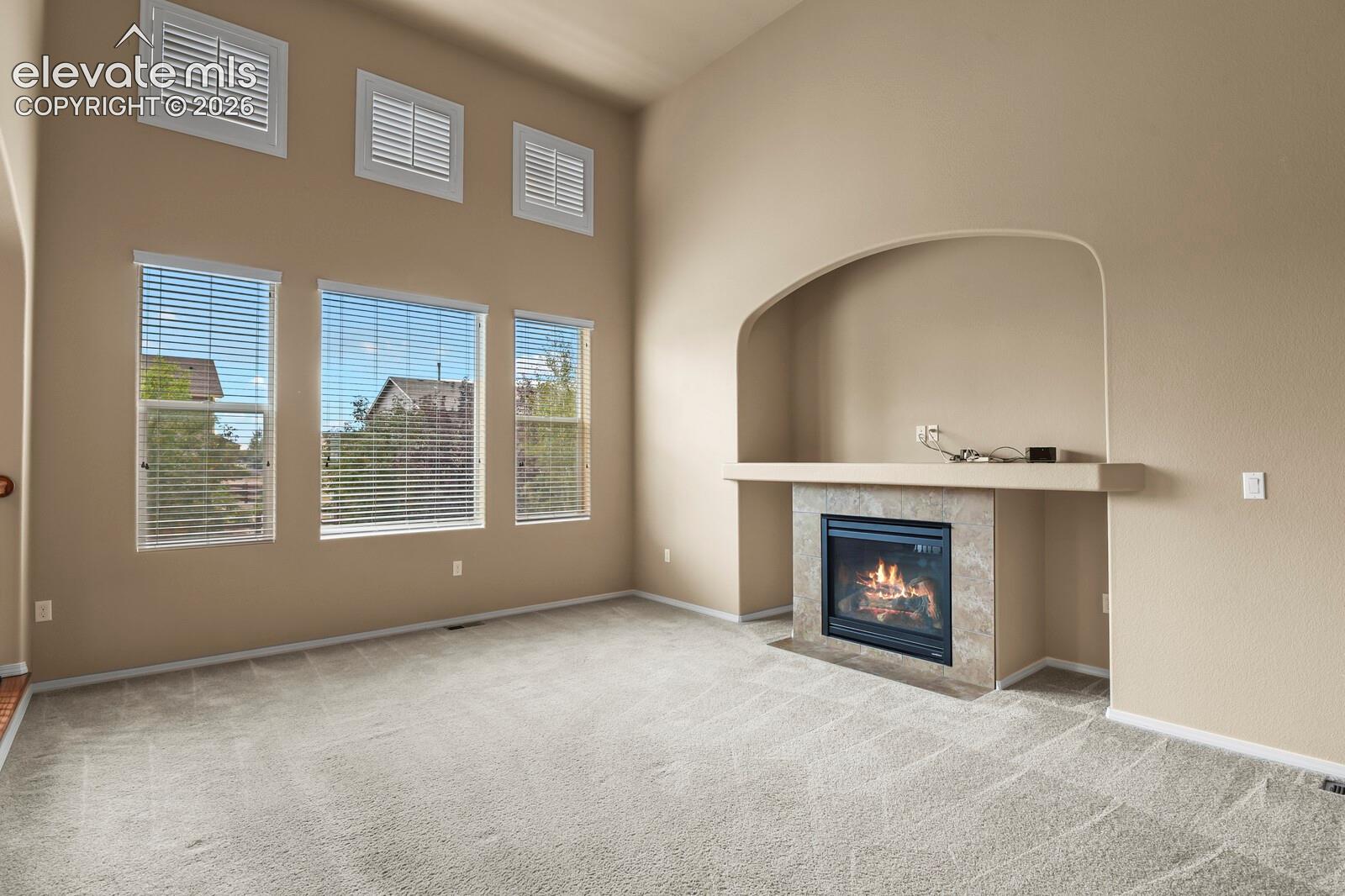 Vaulted ceilings with upper transom windows, a tiled fireplace with mantel, and carpet flooring