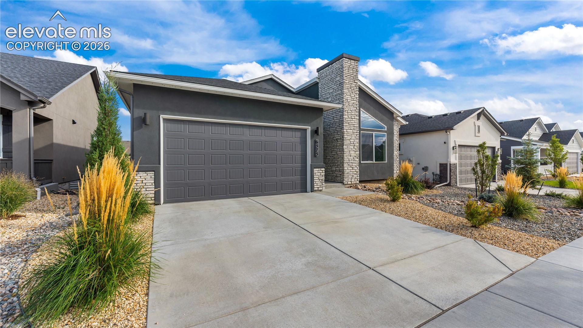 Modern exterior featuring a dark stucco facade, stone veneer chimney, concrete driveway, and xeriscaped front grounds