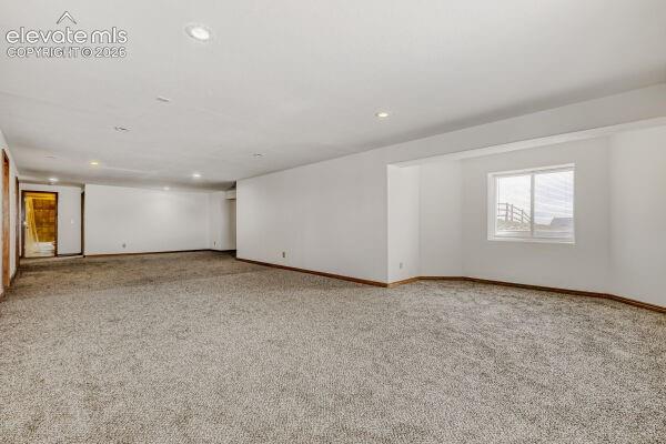 Spacious lower-level room featuring light gray carpeting, recessed ceiling lighting, and crisp white walls