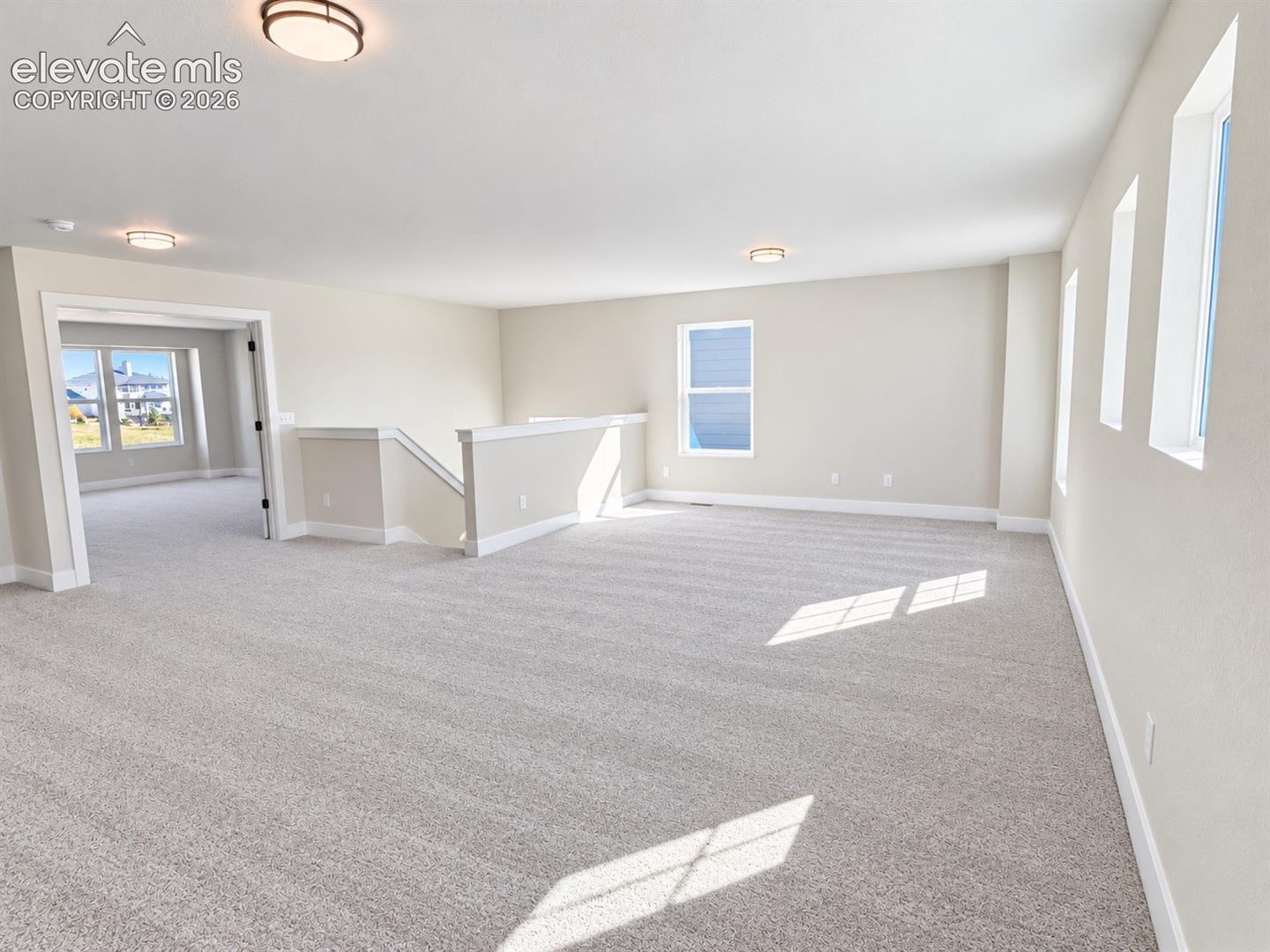 Expansive carpeted space featuring multiple windows, a staircase with a half-wall railing, and flush-mount ceiling lights