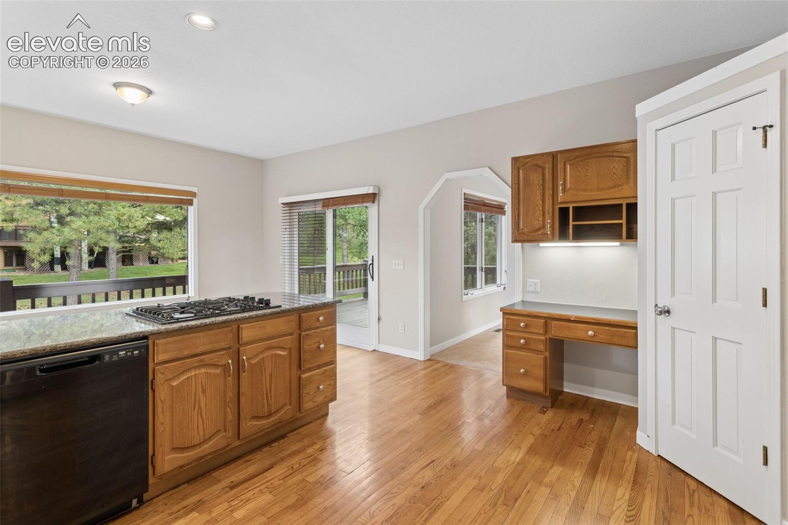 Kitchen island with an integrated gas cooktop, wood-finish flooring, built-in desk with overhead cabinetry, and sliding glass doors to outdoor deck, pantry on the right
