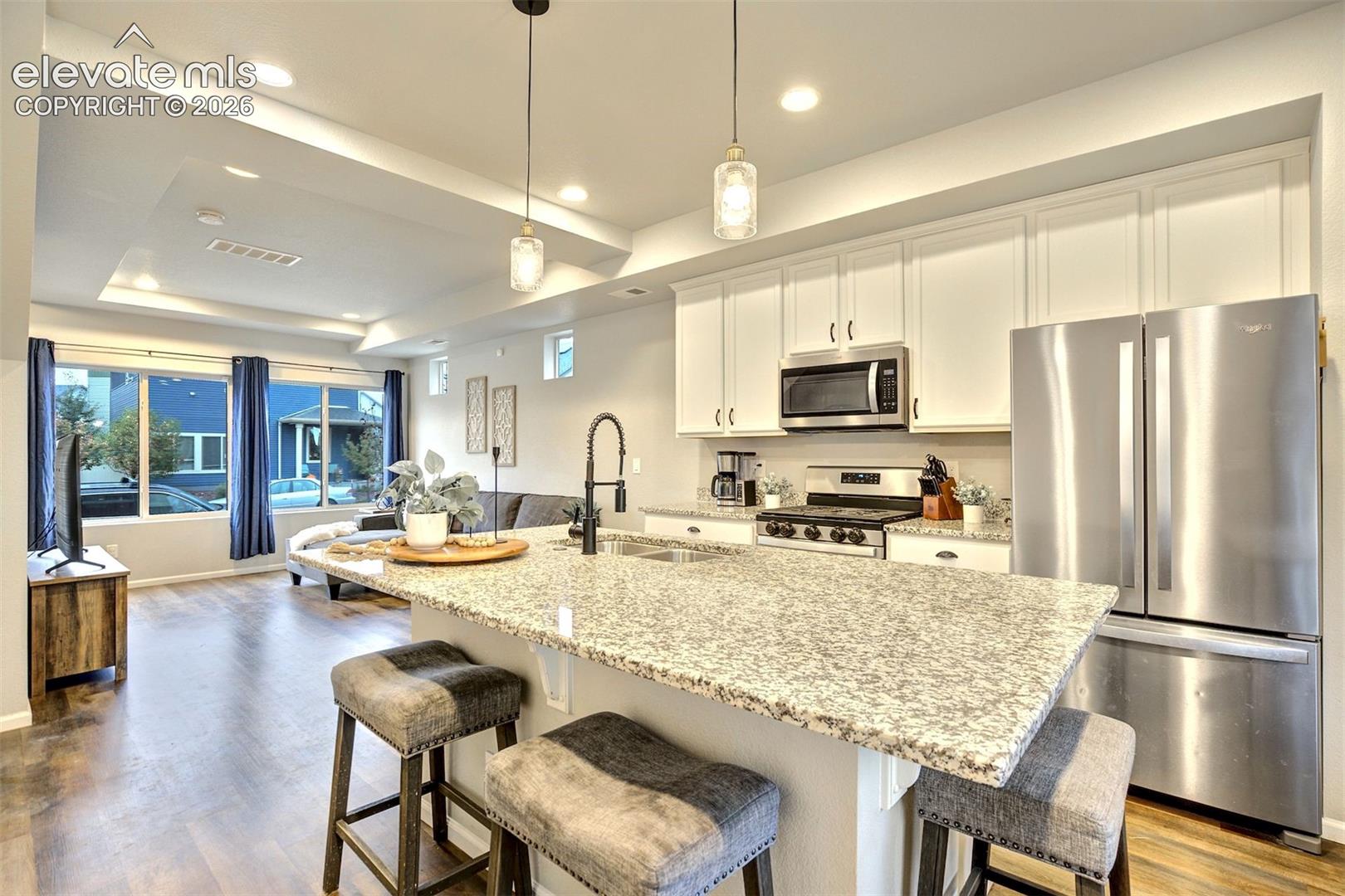 Kitchen featuring a stone-topped island with an integrated sink, white cabinetry, stainless steel appliances, recessed ceiling lighting, and wood-finish flooring