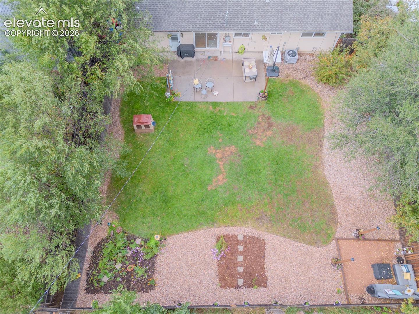 Backyard featuring a concrete patio, grassy lawn, gravel landscape areas, mature trees, and perimeter fencing
