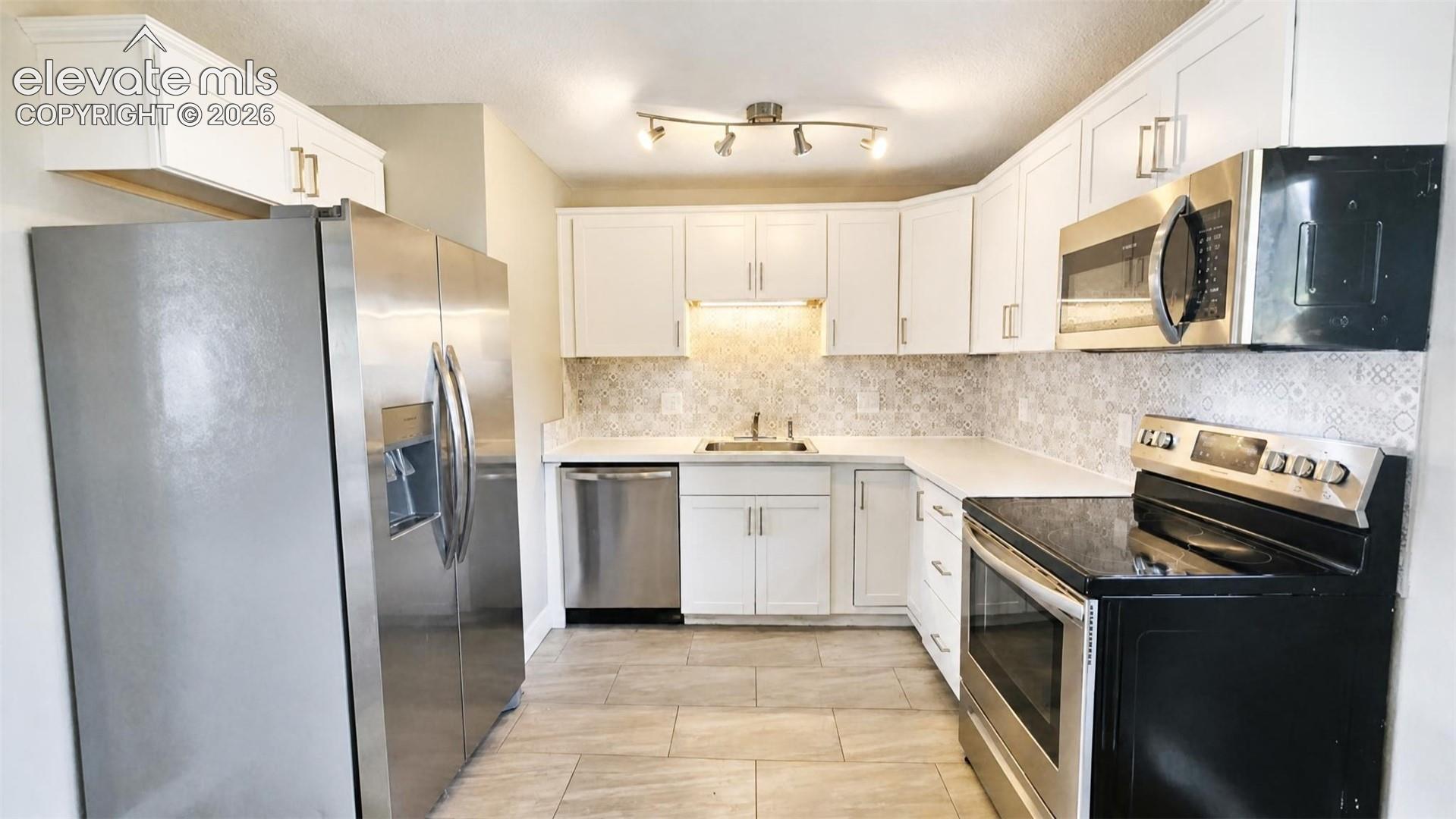 Kitchen featuring white cabinetry, stainless steel appliances, a tile backsplash, and LVP flooring
