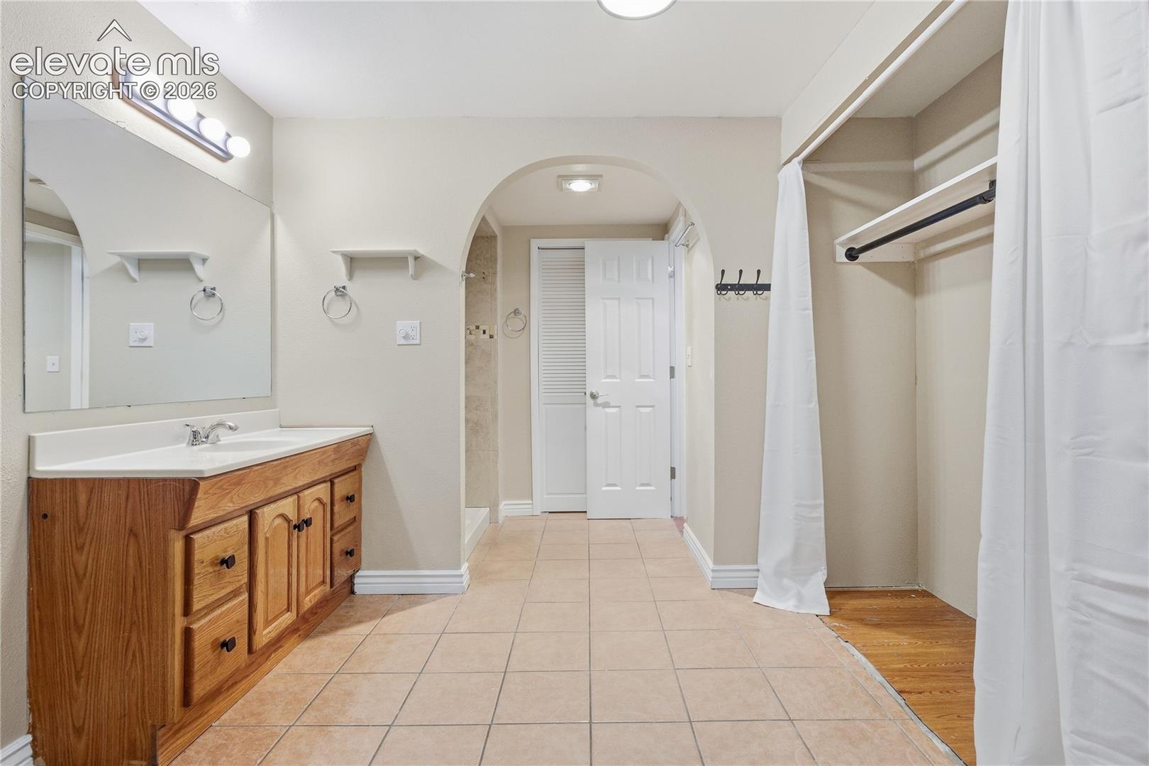 Bathroom featuring a wood-finish vanity with a white countertop and integrated sink, a large wall mirror, and tile flooring
