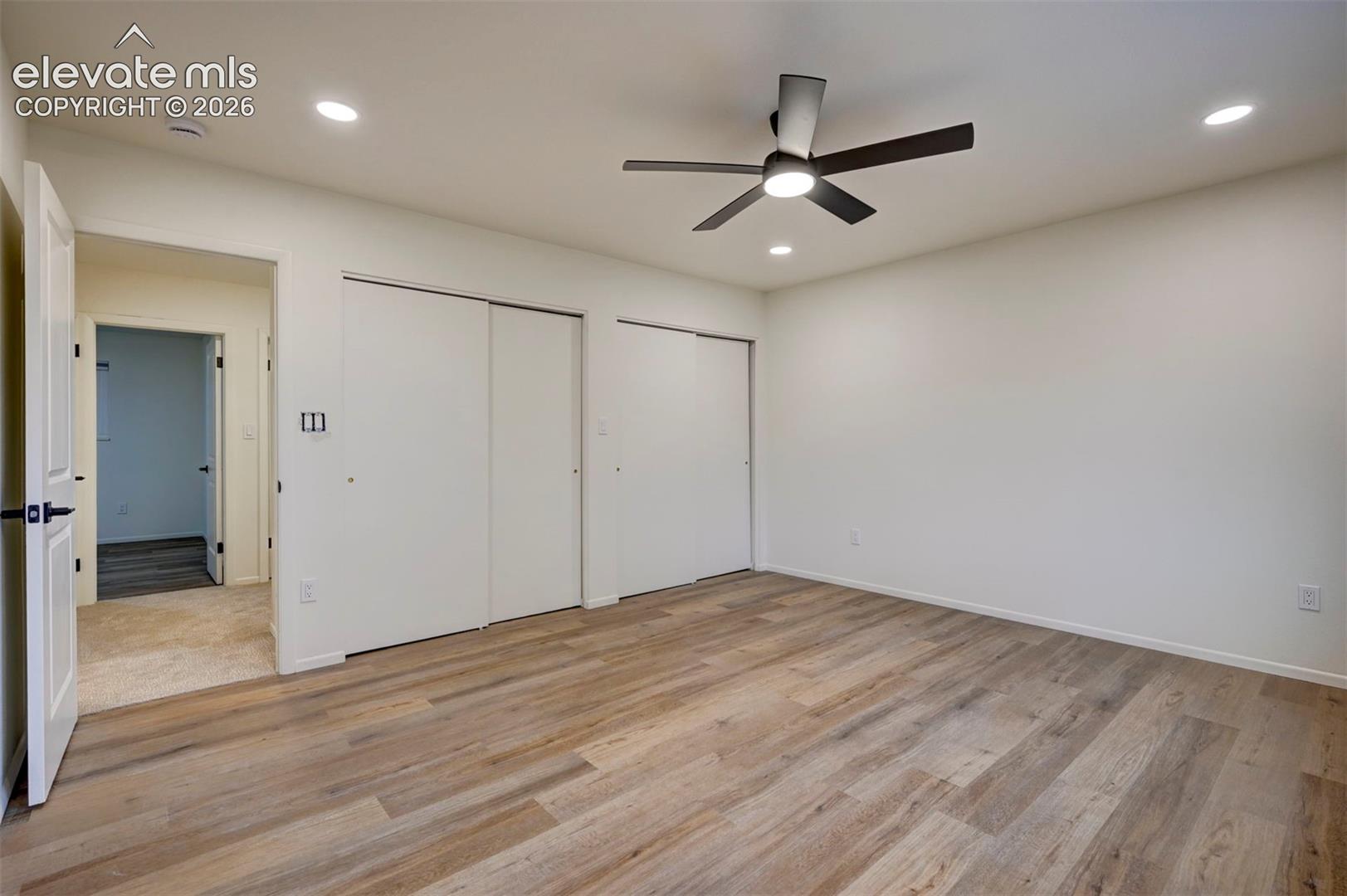 Room featuring wood-finish flooring, dual sliding-door closets, recessed lighting, and a centrally mounted ceiling fan