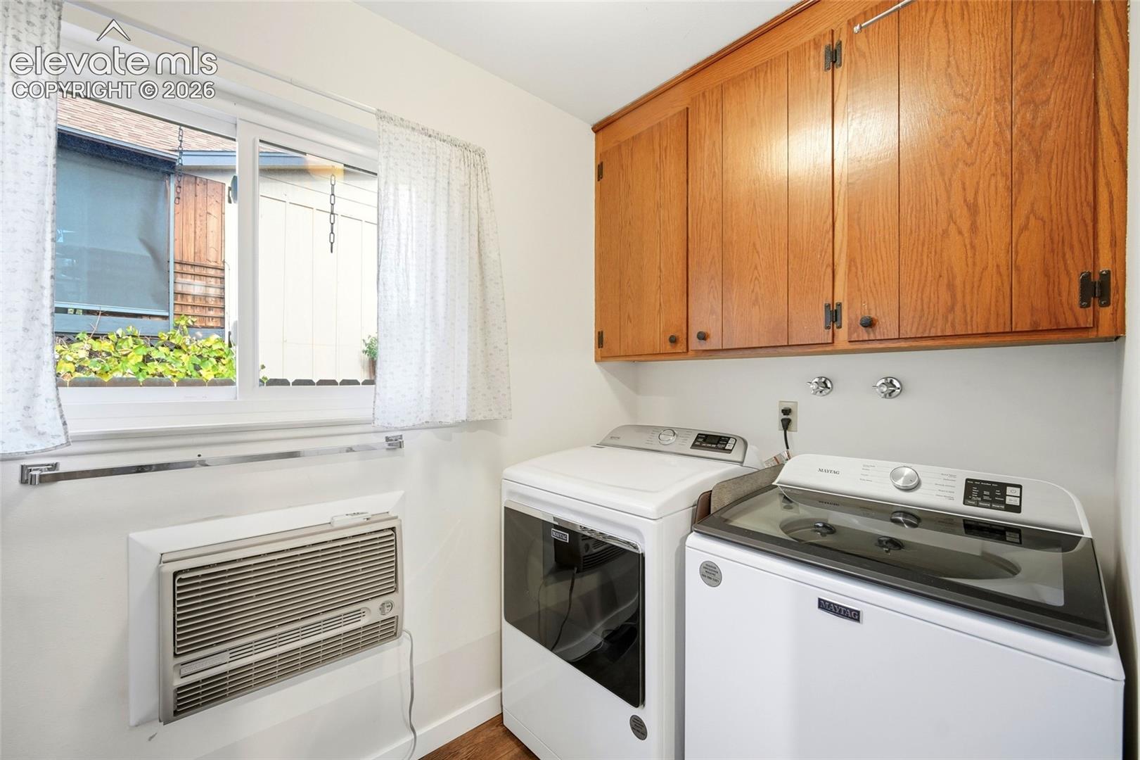 Laundry area featuring wood-finish wall-mounted cabinetry, a sliding window, and a wall-mounted air conditioning unit