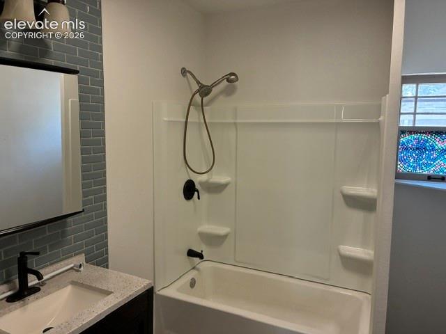 Bathroom featuring a tub/shower combination with a textured surround, a vanity with a white rectangular sink, a light-colored countertop, and a matte black faucet