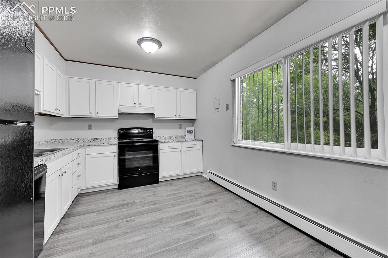 Kitchen with baseboard heating, black appliances, white cabinets, light stone counters, and light wood finished floors