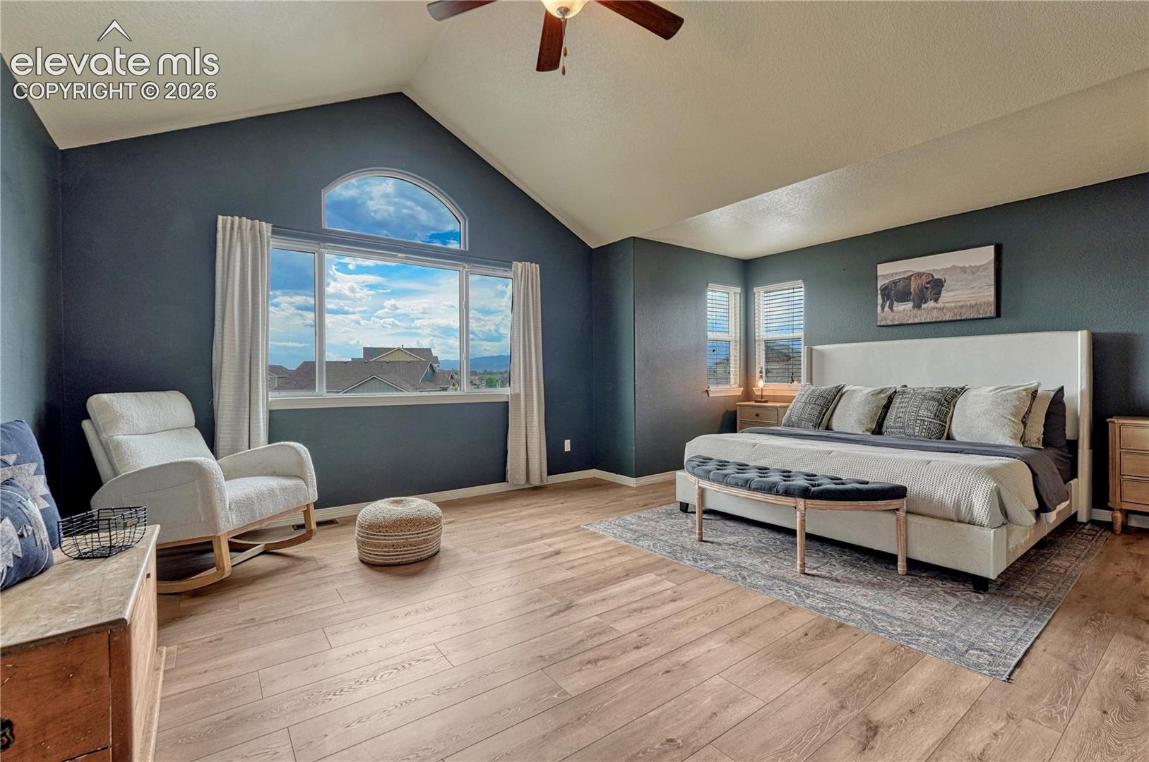Vaulted ceiling with a ceiling fan, arched transom window, large picture window, and wood-finish flooring