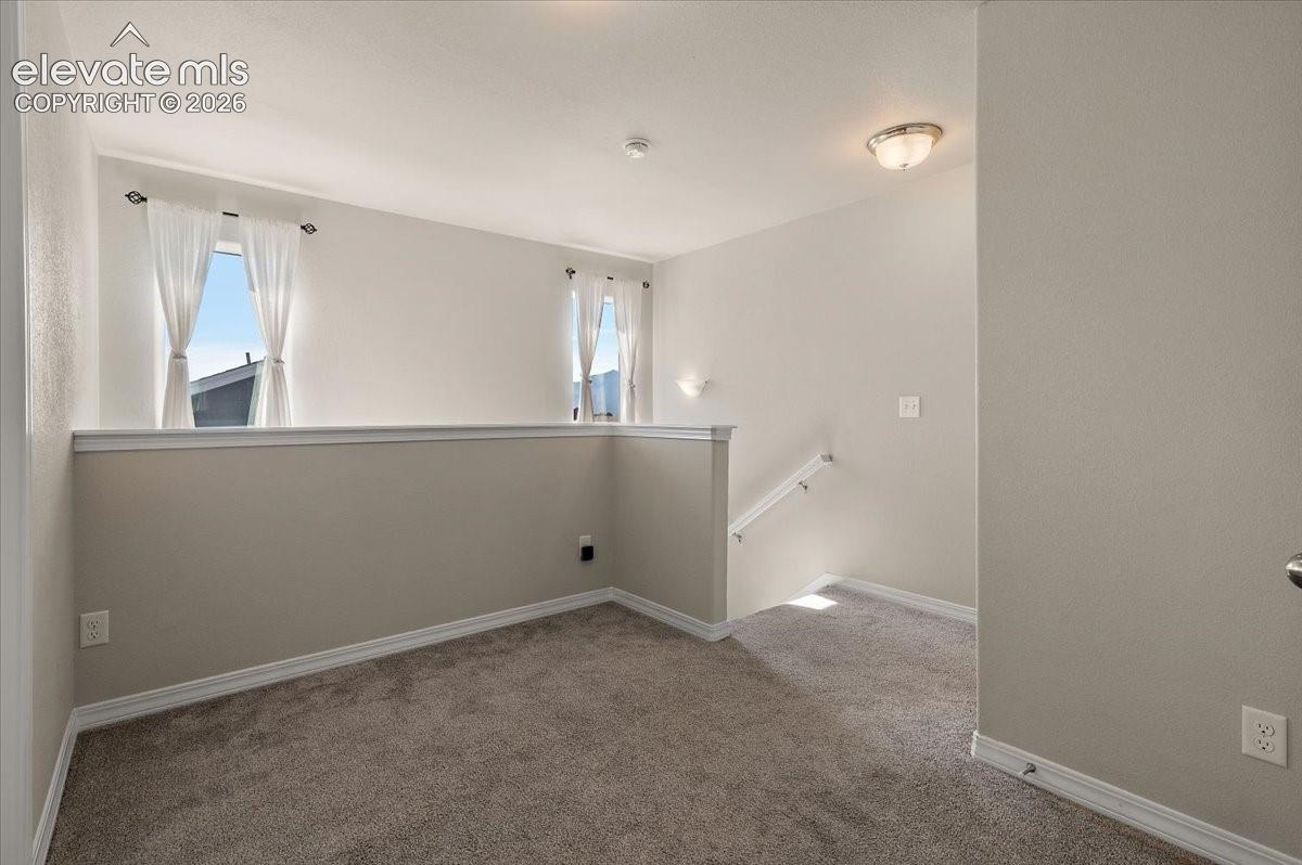 Carpeted open loft area with a partial wall, two windows, and a flush-mount ceiling light
