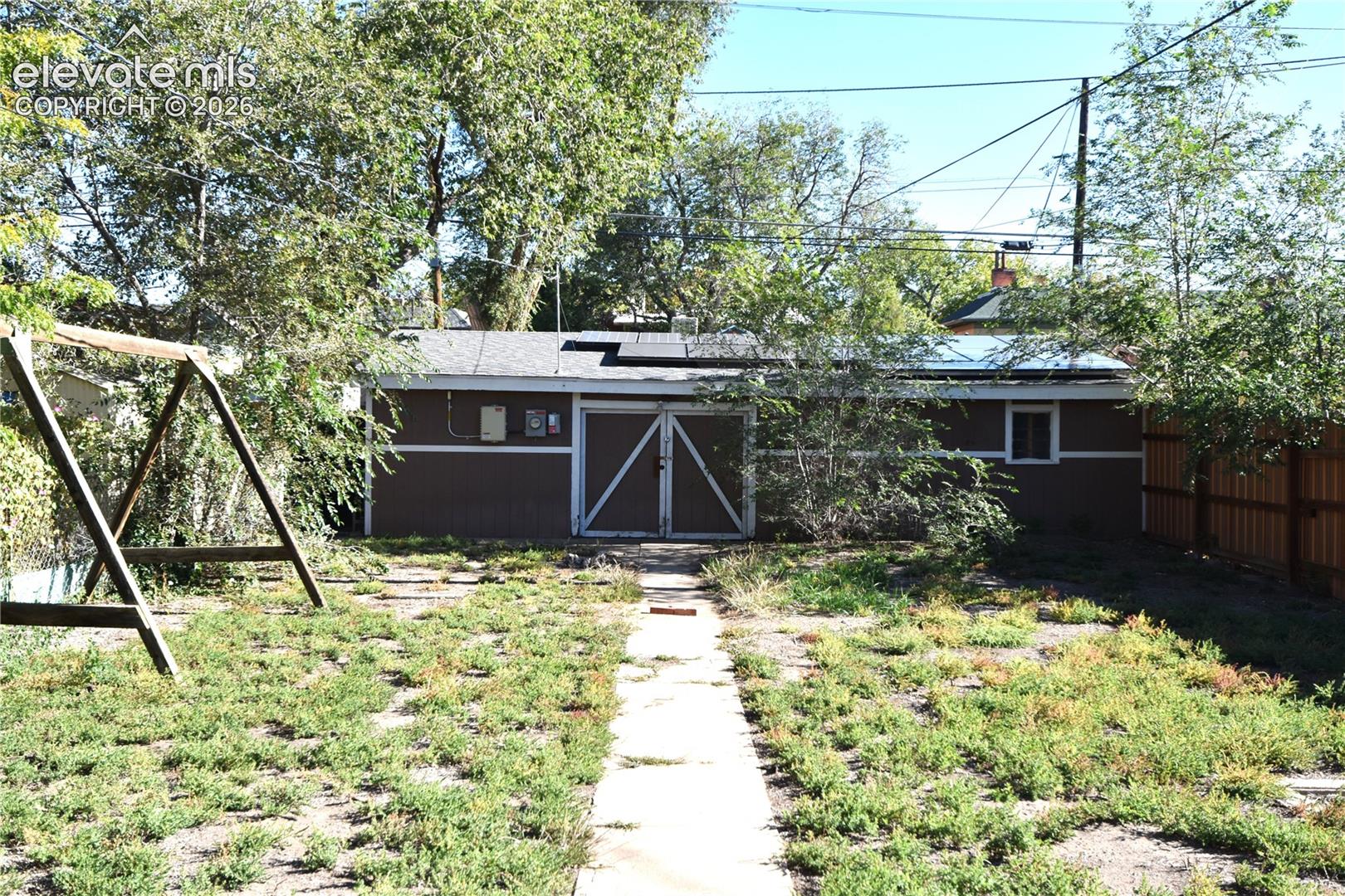 Backyard featuring a detached garage with double doors, solar panels, mature trees, and a concrete pathway