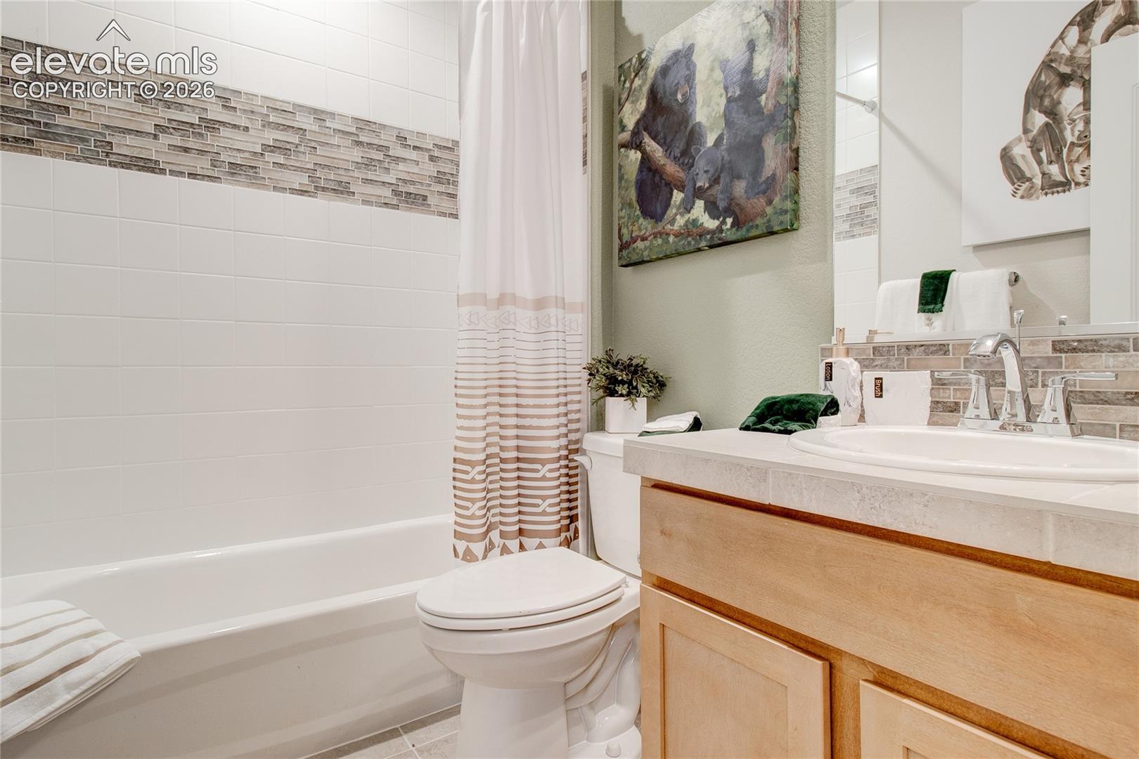 Bathroom featuring a wood-finish vanity with a light-toned countertop, integrated basin, chrome fixtures, and a shower-tub combination with horizontal tile backsplash