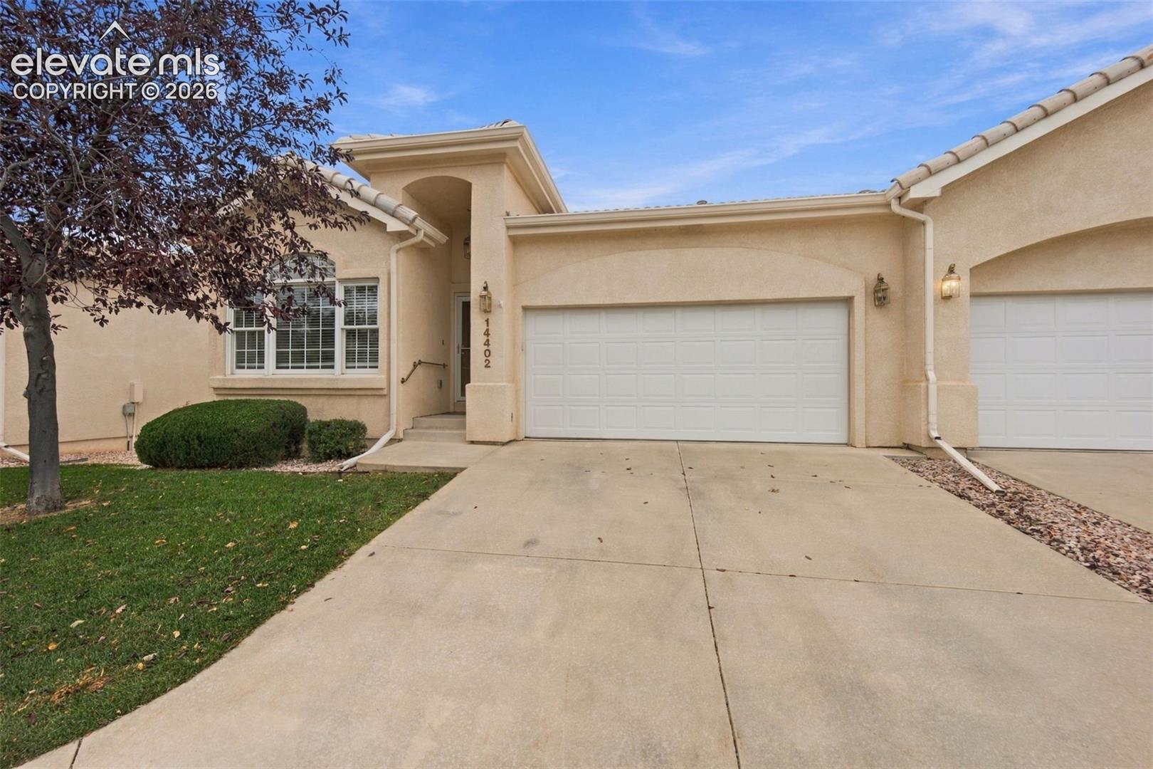 Stucco exterior with multi-car garage, concrete driveway, arched entry, and grid-pattern window detailing