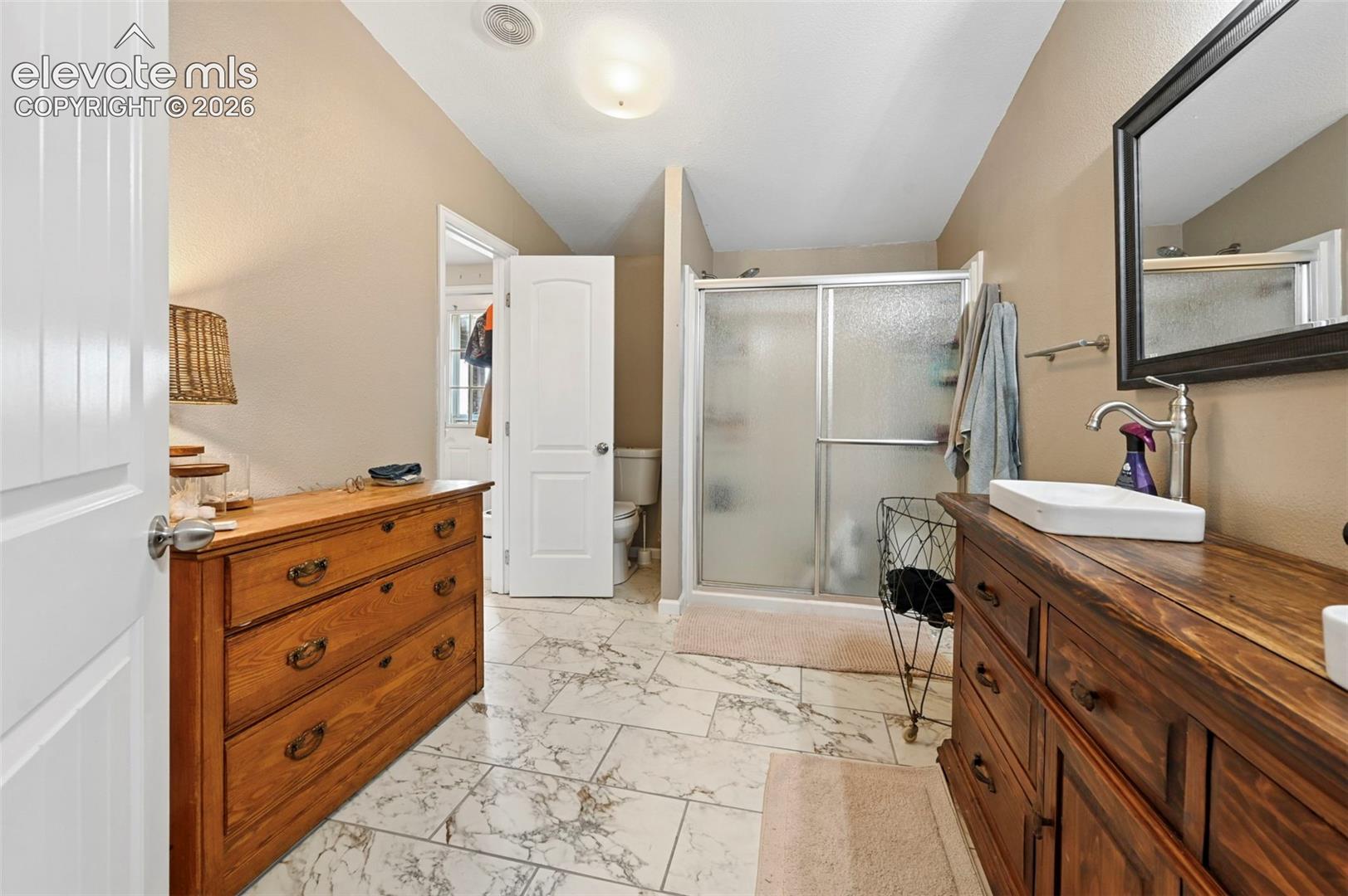 Bathroom featuring large-format tile flooring, a wood-finish vanity with a rectangular vessel sink, and a walk-in shower with a sliding glass enclosure