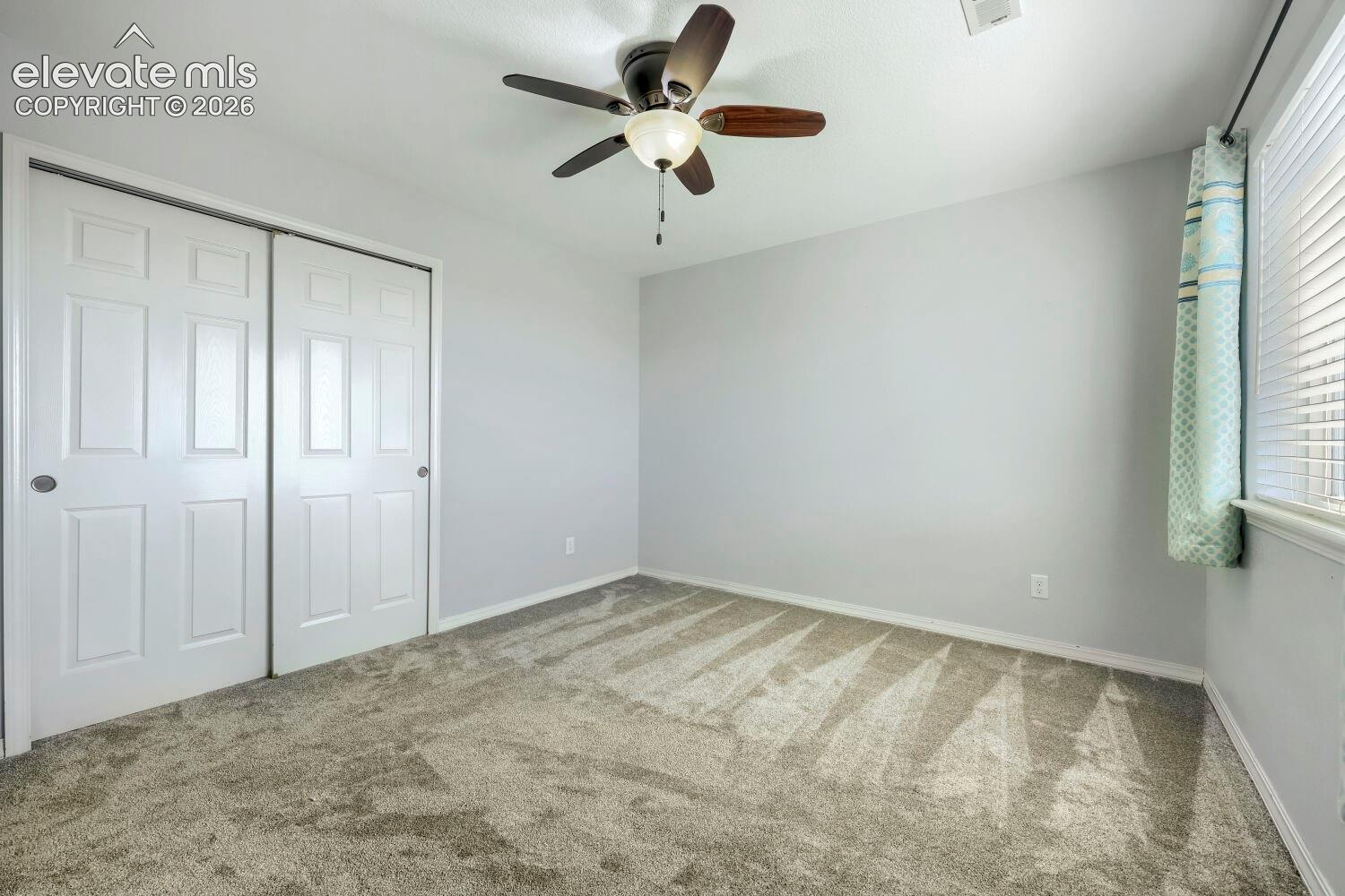 Neutral-toned carpeting, ceiling fan with integrated light fixture, and dual-panel sliding closet doors