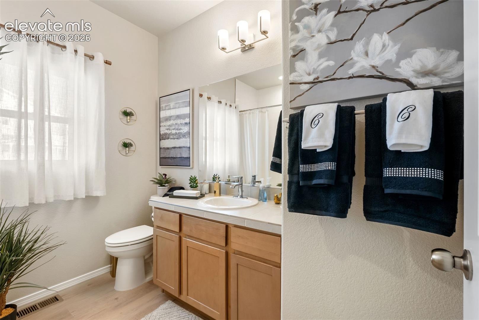 Bathroom featuring a vanity with wood-finish cabinetry, a white countertop with an integrated basin, a polished chrome faucet, a wall-mounted light fixture, and a large mirror