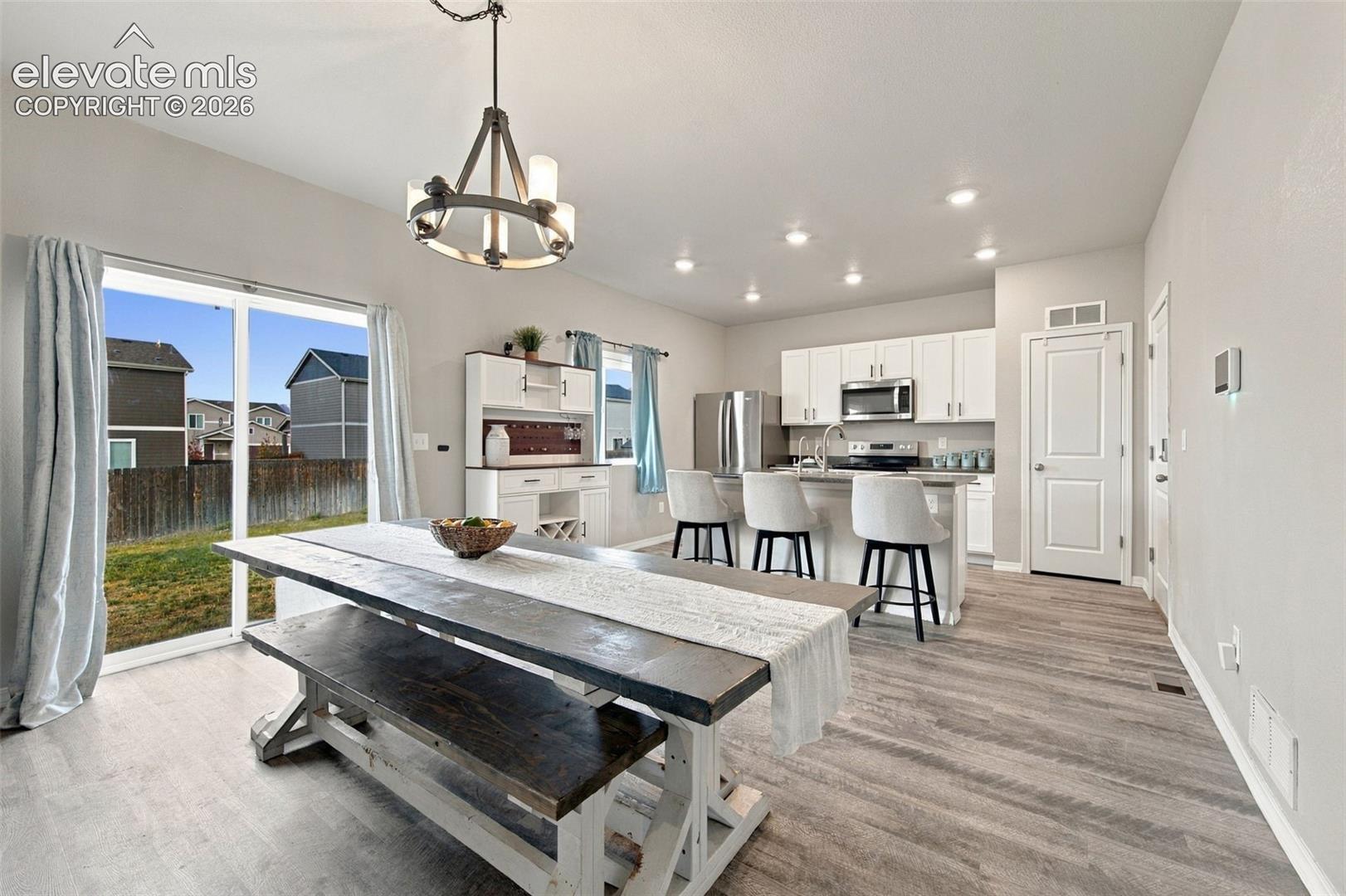 Kitchen featuring white cabinetry, stainless steel appliances, a central island with counter seating, wood-finish flooring, and a metal chandelier fixture