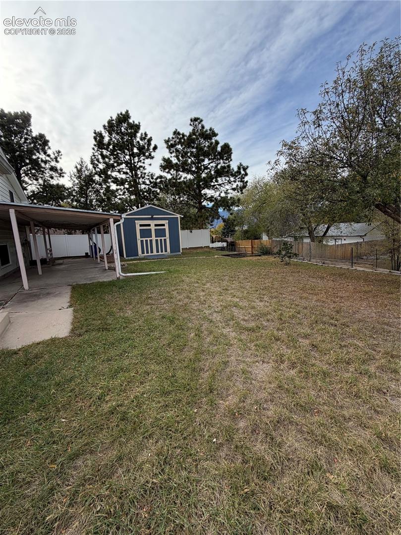Expansive backyard featuring a covered concrete patio, detached storage shed, perimeter fencing, and mature trees
