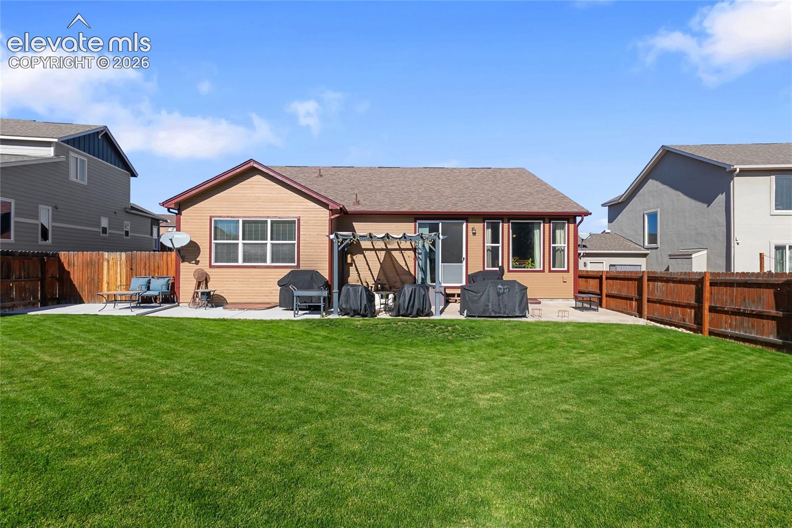 Backyard featuring a manicured lawn, concrete patio, wooden perimeter fencing, and a built-in pergola