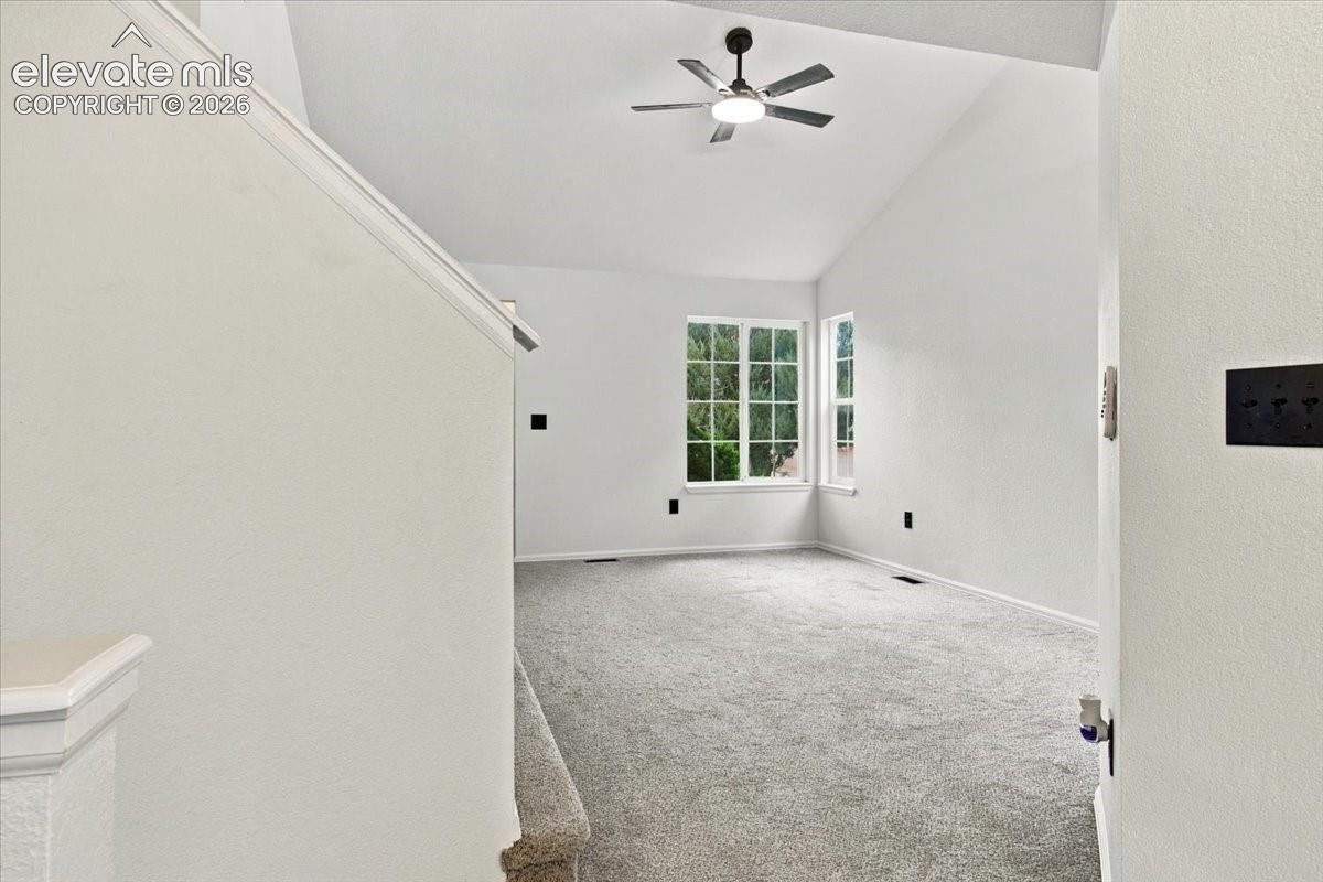 Vaulted ceilings with a central ceiling fan, neutral wall-to-wall carpeting, and multi-pane windows