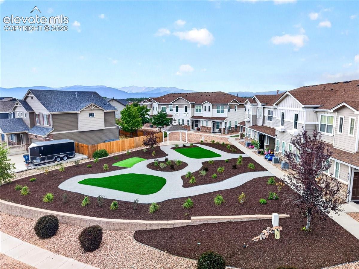Community green space featuring artificial turf areas, paved pathways, and landscaped planting beds