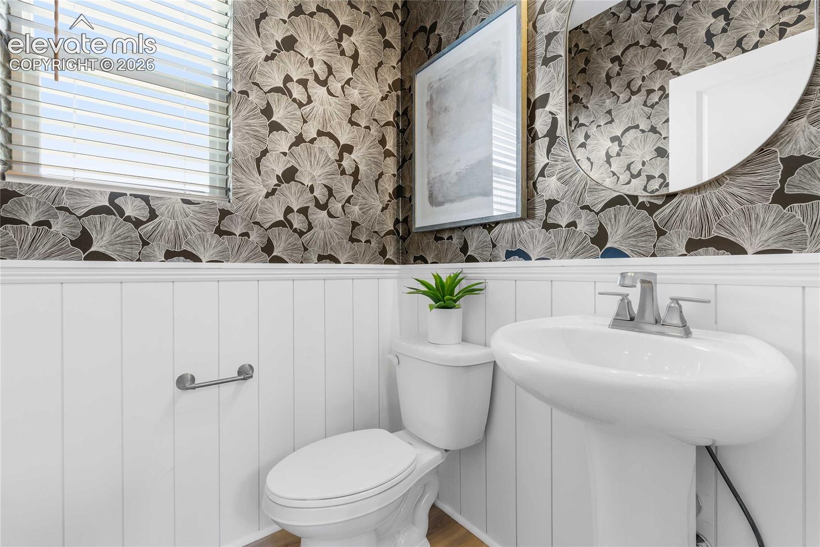 Pedestal sink with a chrome faucet, white paneling, and patterned wallpaper
*photos of a model home*