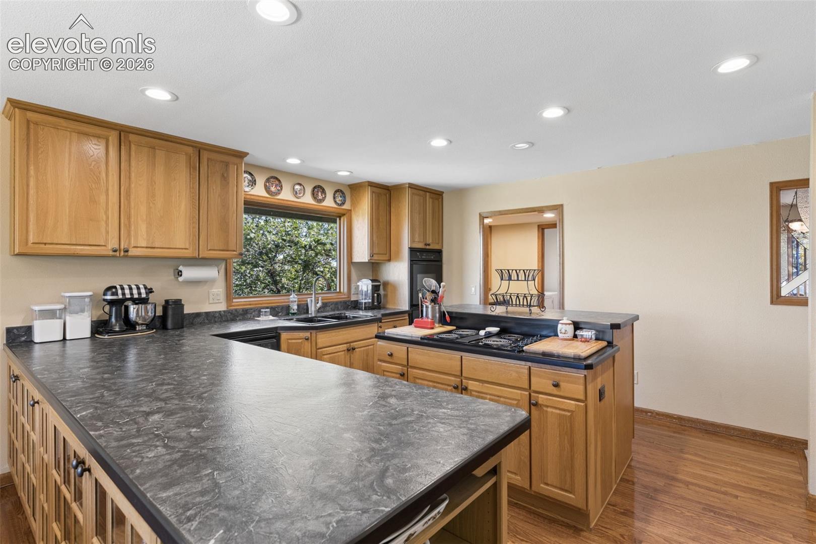 Kitchen featuring wood cabinetry, dark stone-finish countertops, recessed lighting, wood-finish flooring, and a built-in cooktop island