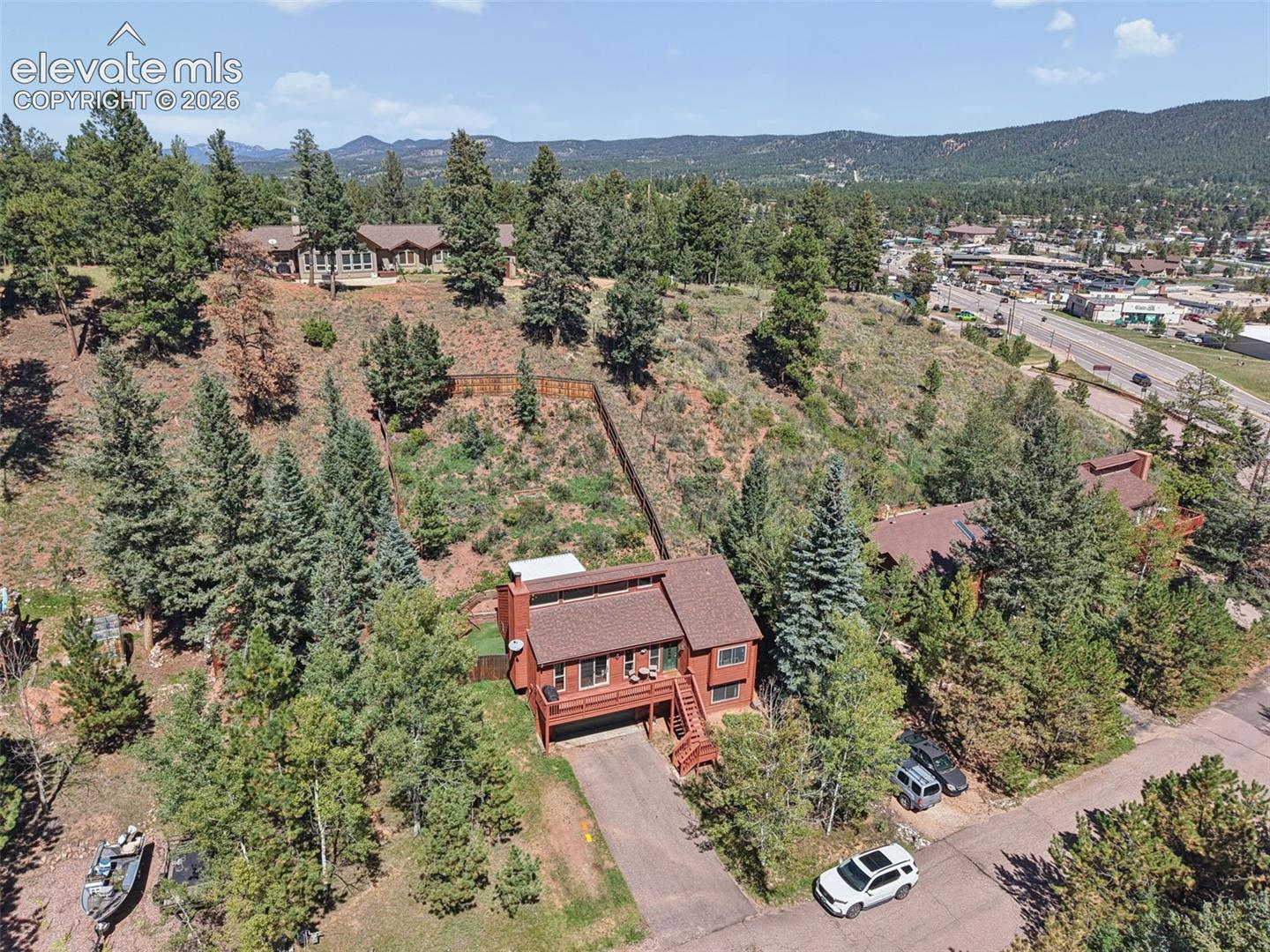 Multi-level residence featuring a brown shingled roof and exterior, an attached garage, and surrounding mature trees