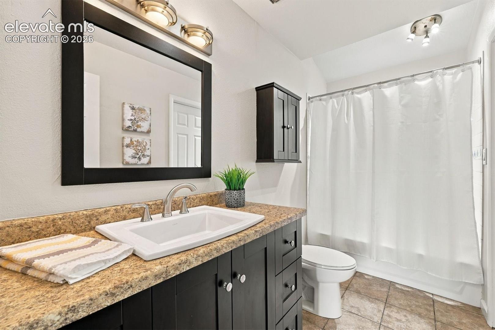 Bathroom featuring a dark-finish vanity with a drop-in sink, stone-composite countertop, matching wall-mounted medicine cabinet, framed mirror, and tile flooring