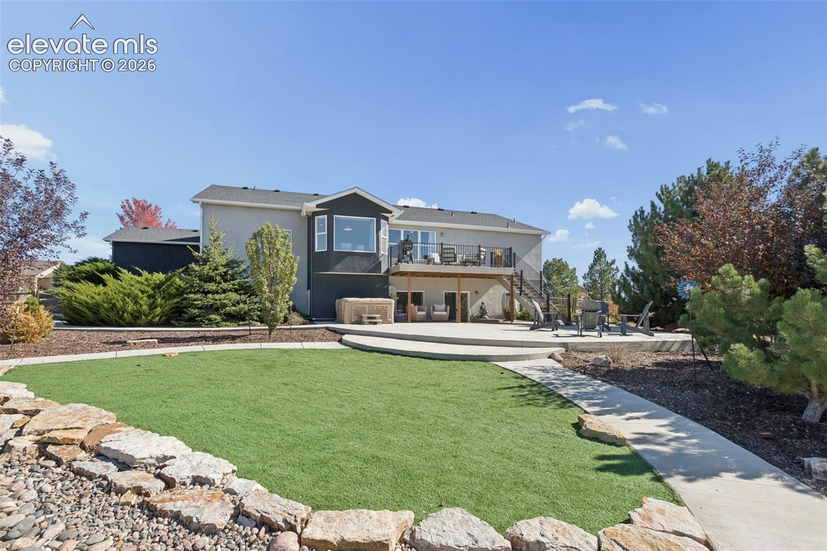Expansive backyard featuring a manicured lawn, concrete patio, and upper-level deck with black railings