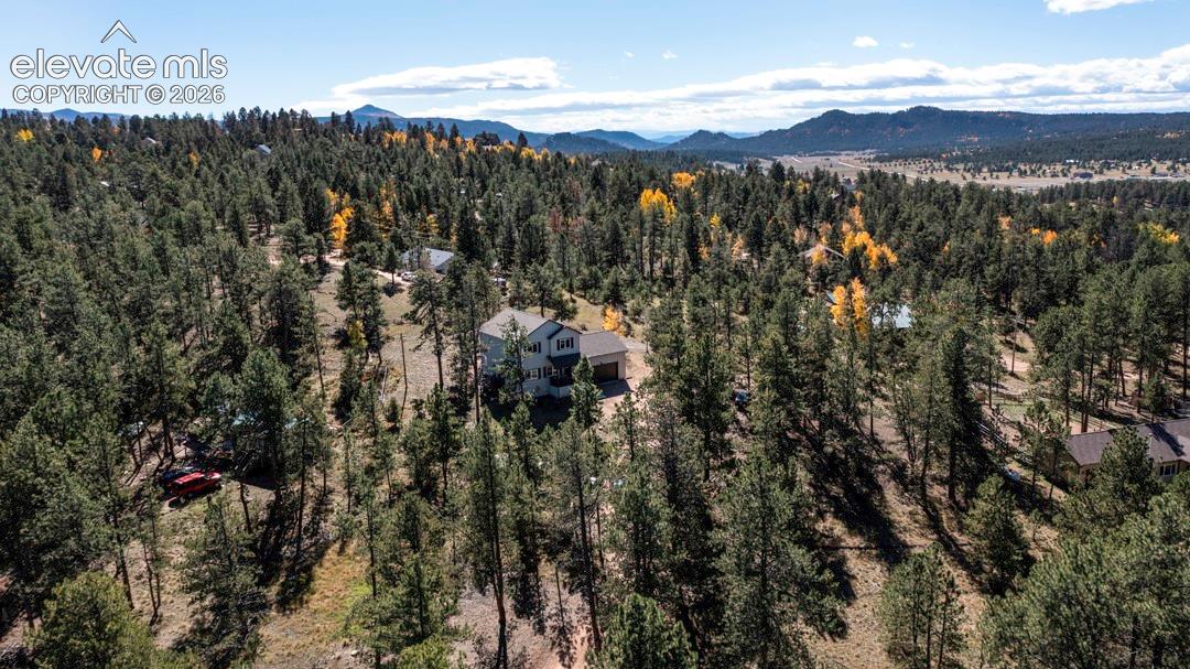 Aerial perspective of a detached multi-level residence situated within a heavily wooded lot featuring mature coniferous trees and mountain topography
