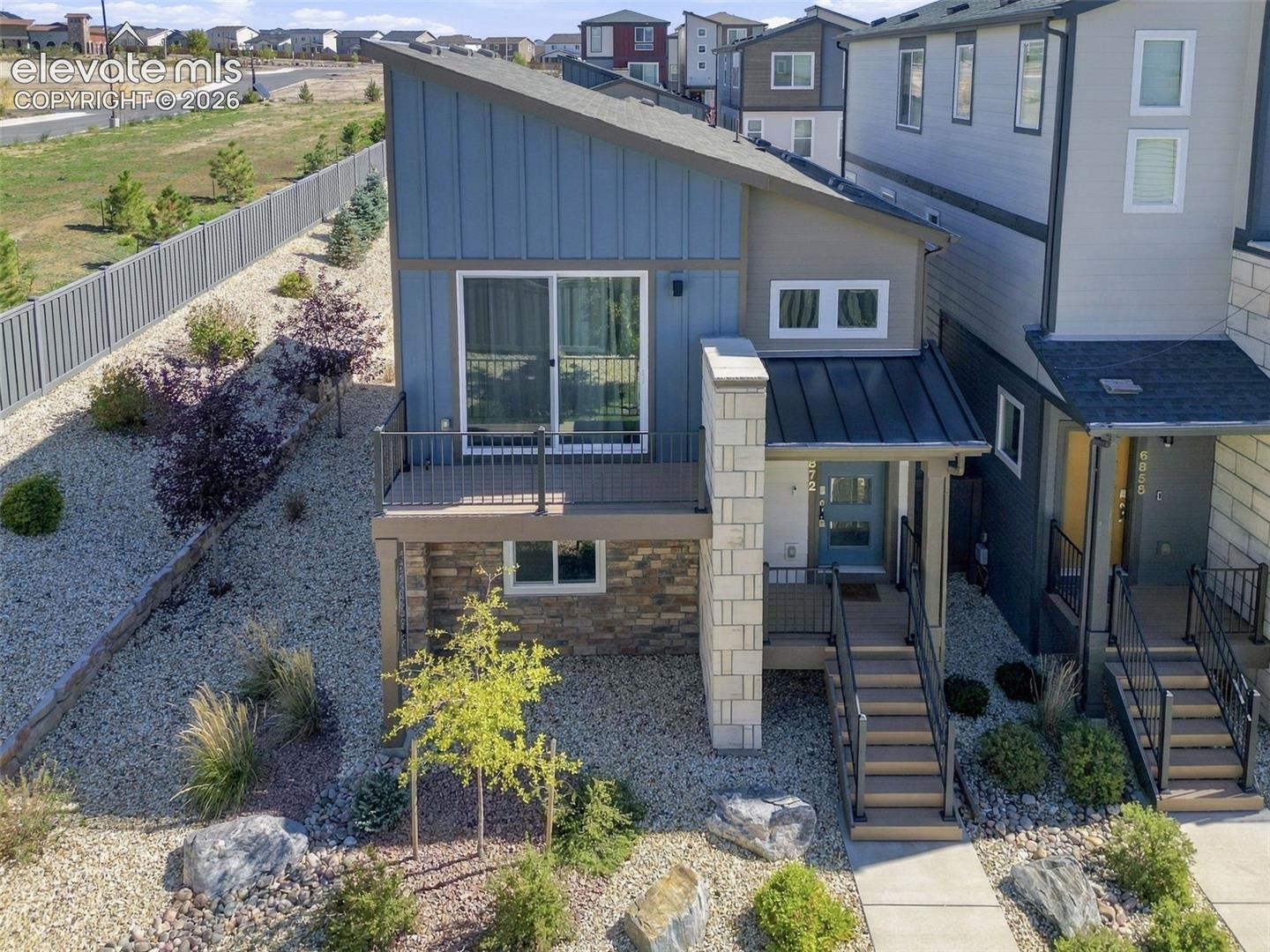 Contemporary multi-level exterior featuring vertical siding, stone veneer accents, a metal roof, and an elevated deck with metal railings