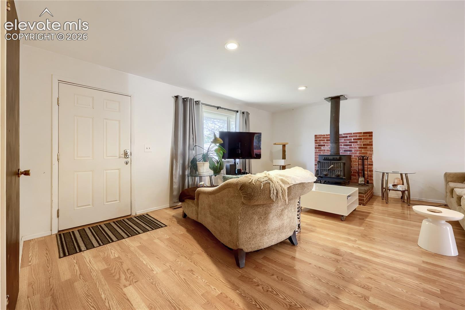 Living area featuring wood-finish flooring, recessed lighting, and a brick-surround wood-burning stove on a stone hearth