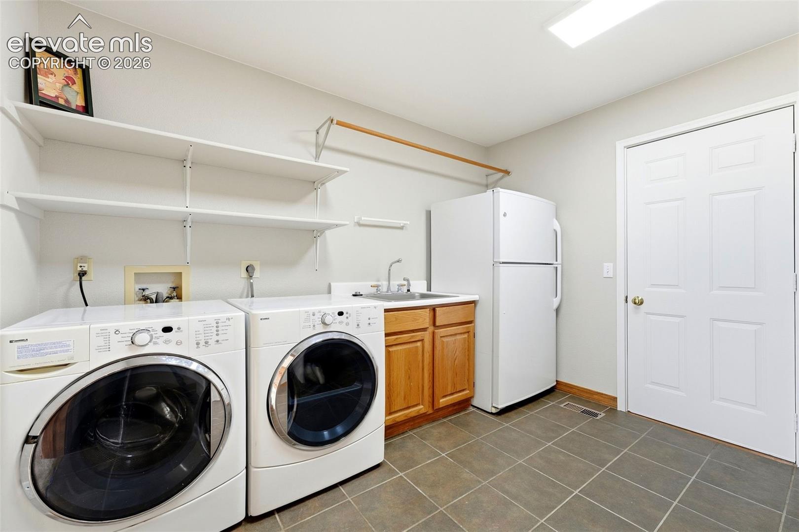Tile flooring, built-in shelving, wood-finish cabinetry, utility sink, and recessed lighting