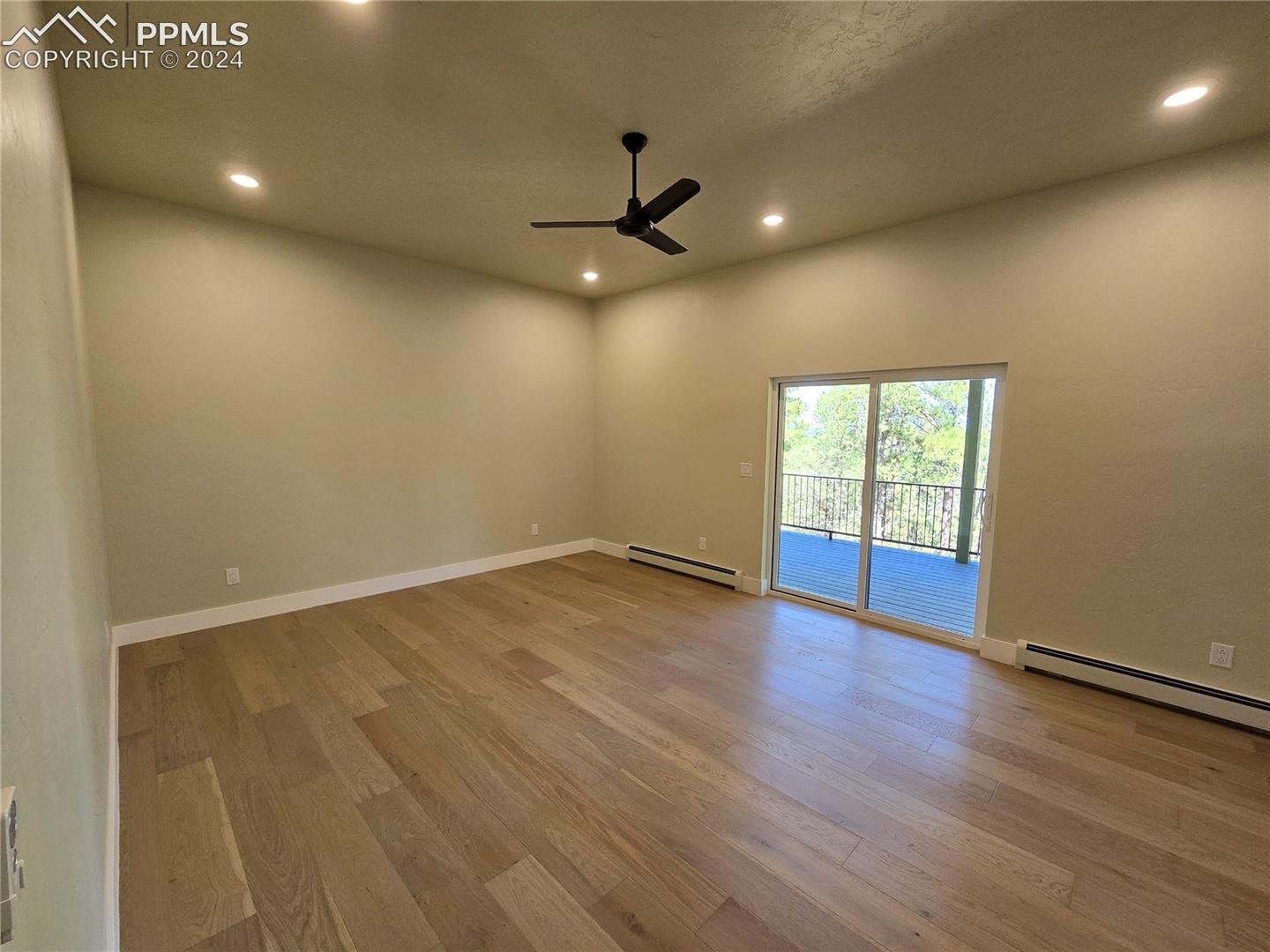 Primary bedroom with a textured ceiling, baseboard heating, ceiling fan, and light hardwood / wood-style floors and sliding door to deck.