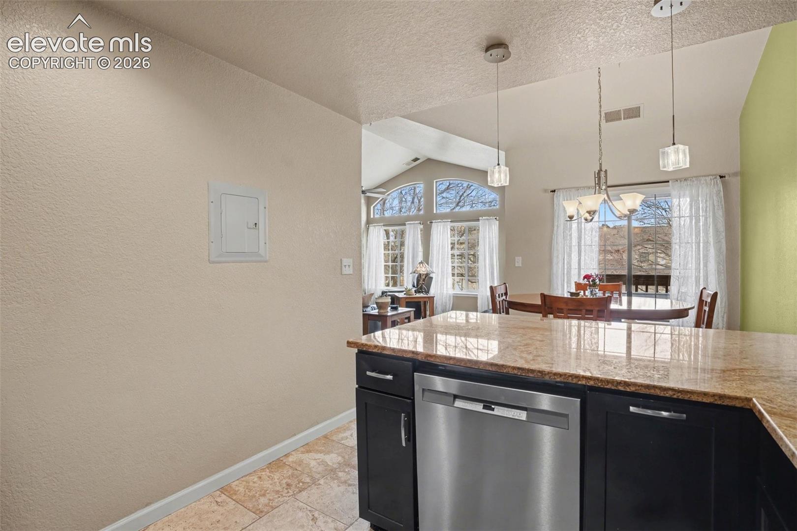 Kitchen featuring stone-finish countertops, stainless steel dishwasher, dark cabinetry, and tile flooring, accented by pendant lighting