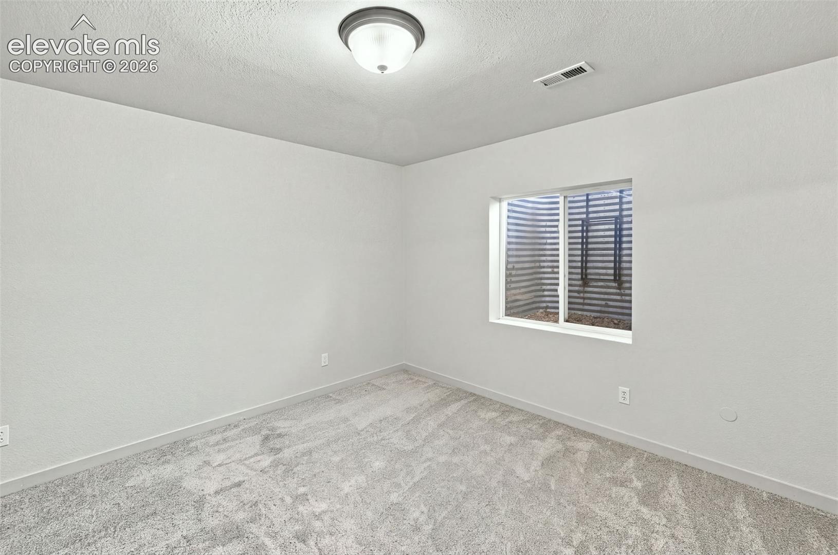 Neutral-toned carpeting, crisp white walls, and a recessed window well featuring a metal egress ladder and sliding window
