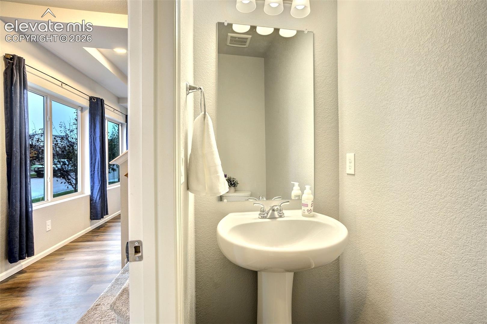 Powder room featuring a white pedestal sink, chrome hardware, a rectangular wall-mounted mirror, and a three-bulb vanity light fixture