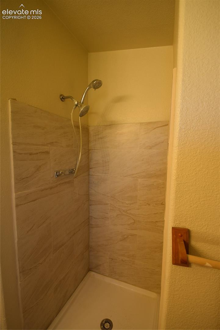 Tiled shower stall featuring a showerhead with an attached handheld sprayer