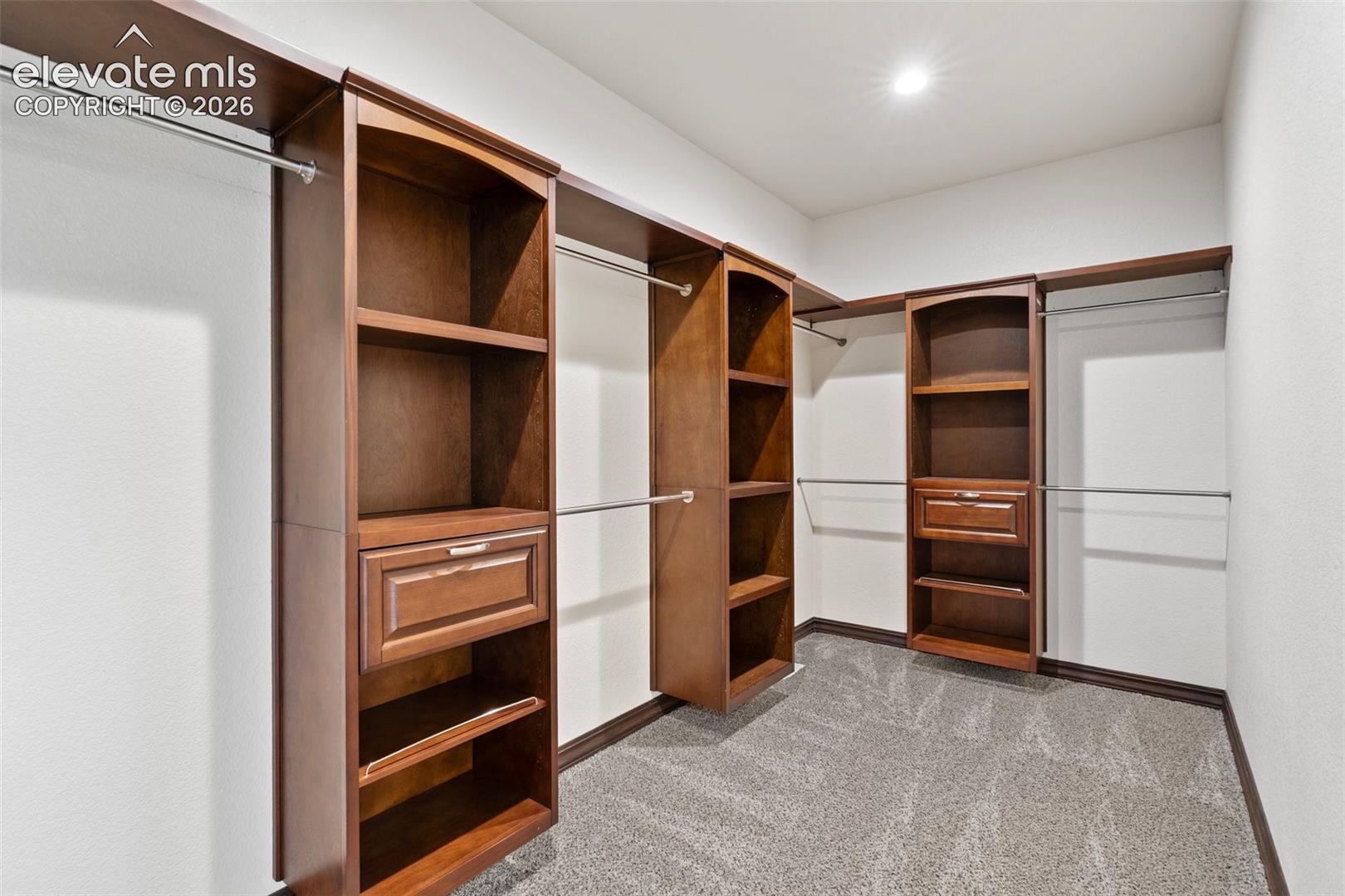 Walk-in closet featuring built-in wood-finish cabinetry, chrome hanging rods, recessed lighting, and textured carpet flooring