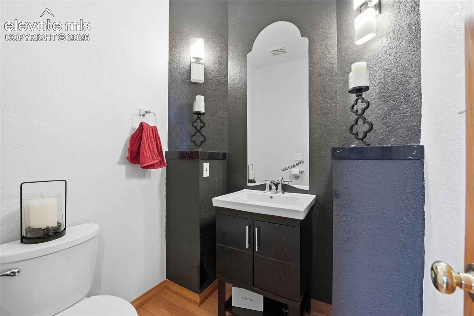 Pedestal sink with chrome faucet, arched mirror, wall-mounted sconces, and wood-finish flooring